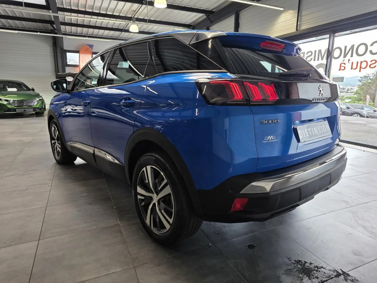 Peugeot 3008 bleu Iron vue 3/4 arrière droit en showroom, avec jantes alliage bi-ton et feux LED distinctifs.