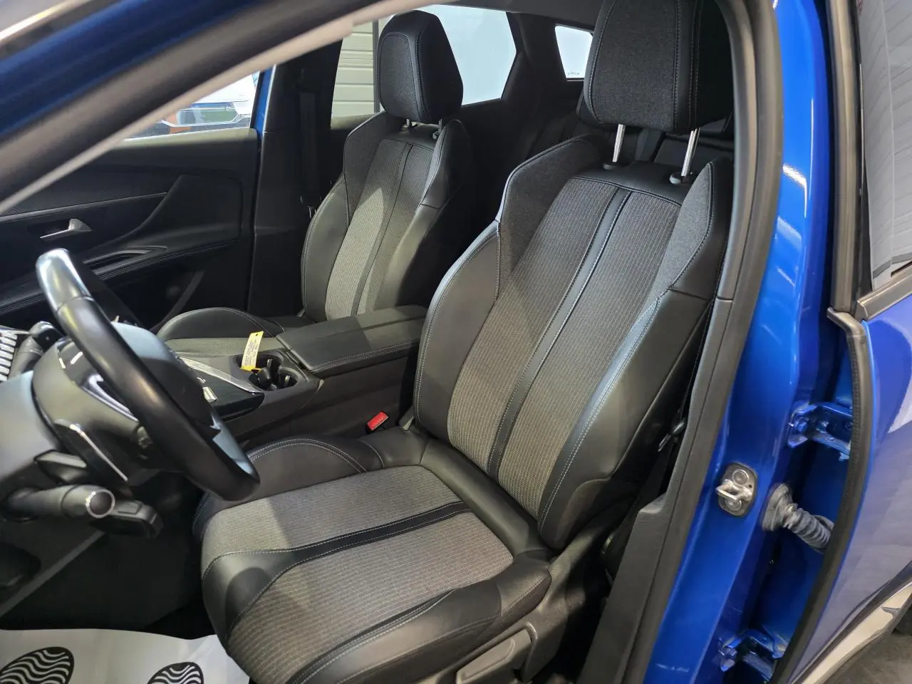 Vue intérieure côté conducteur du Peugeot 3008 Bleu Iron 2022, sièges en tissu et cuir TEP bicolore avec accoudoir central ouvert.