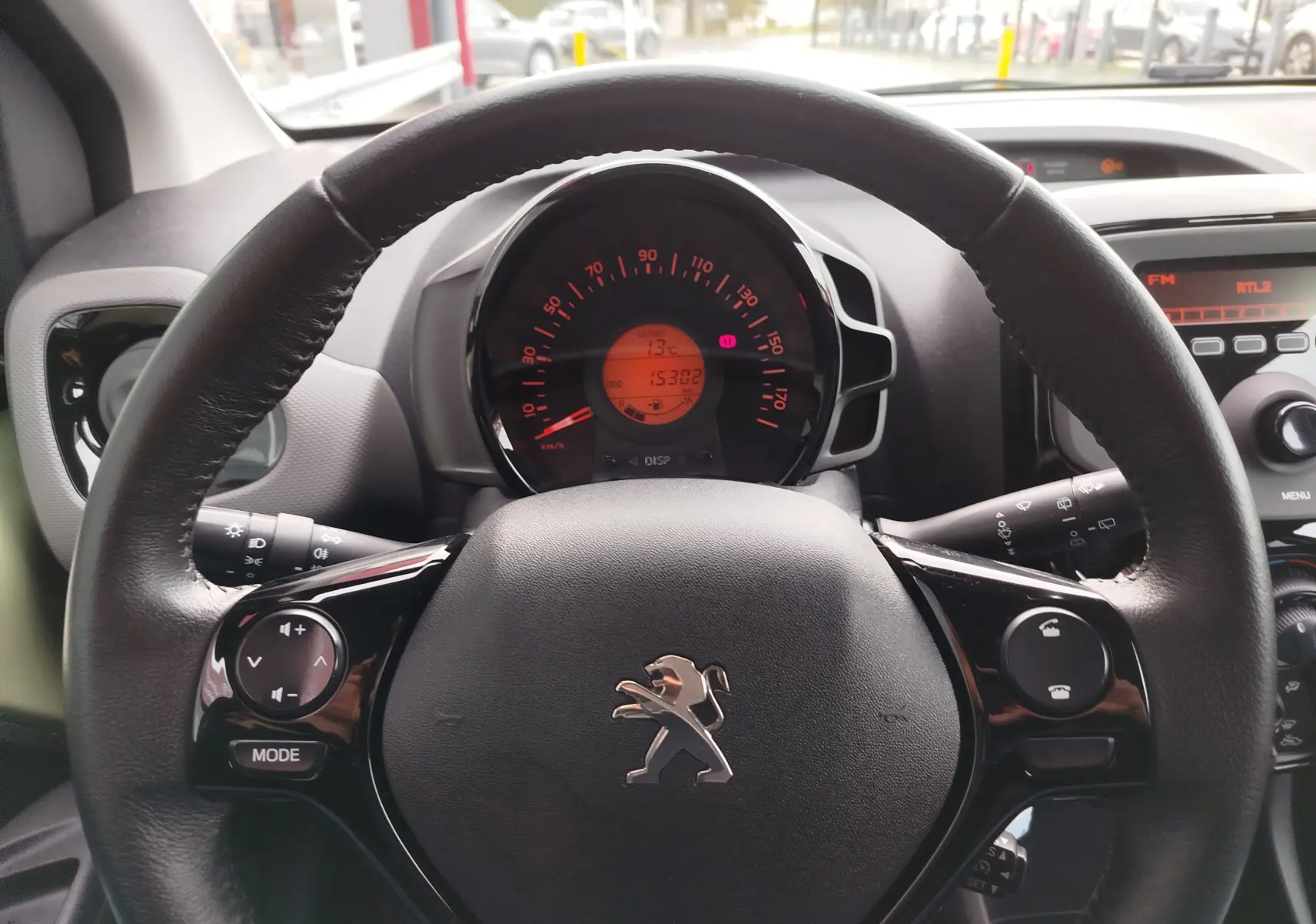 Vue rapprochée du volant en cuir noir avec logo Peugeot et tableau de bord numérique allumé d'une 108 2021.