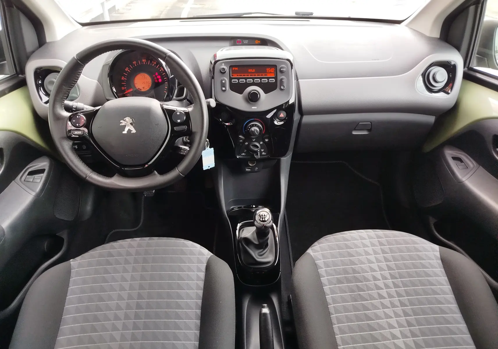 Vue intérieure avant de la Peugeot 108 2021, volant multifonction, tableau de bord noir et sièges gris à motifs géométriques.