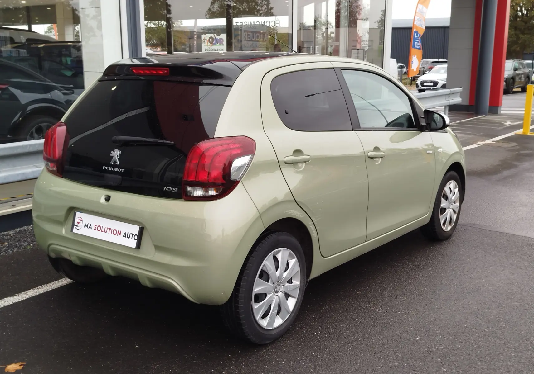 Vue 3/4 arrière droite d'une Peugeot 108 Smooth Green 2021 avec vitre arrière noire et feux arrière rouges.