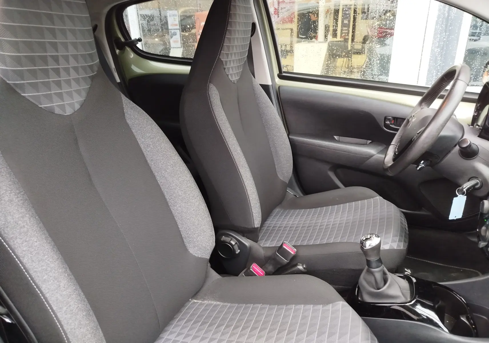 Vue intérieure côté conducteur de la Peugeot 108 2021, sièges tissu gris à motifs géométriques et volant multifonction.