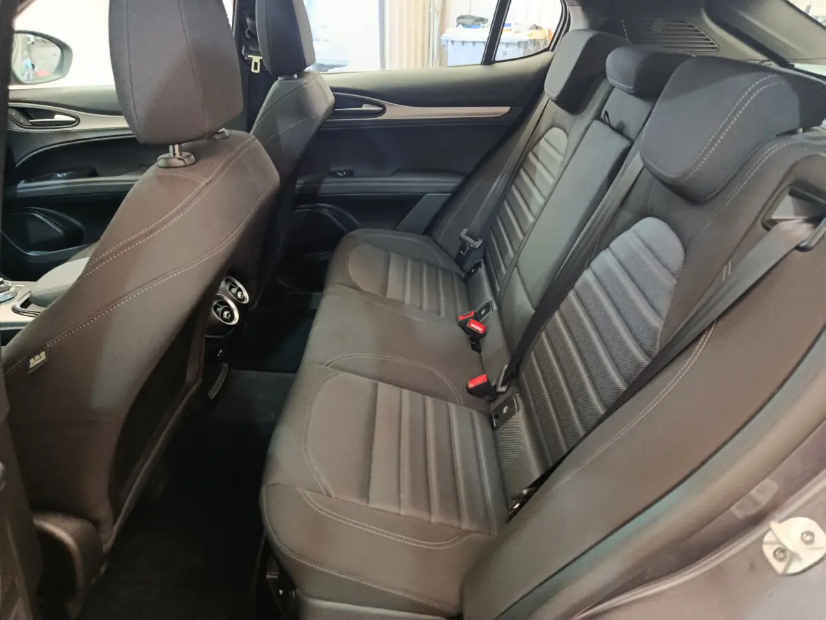 Vue latérale droite de l'habitacle arrière de l'Alfa Romeo Stelvio Sprint 2024 avec sièges tissu gris foncé et ceintures visibles.