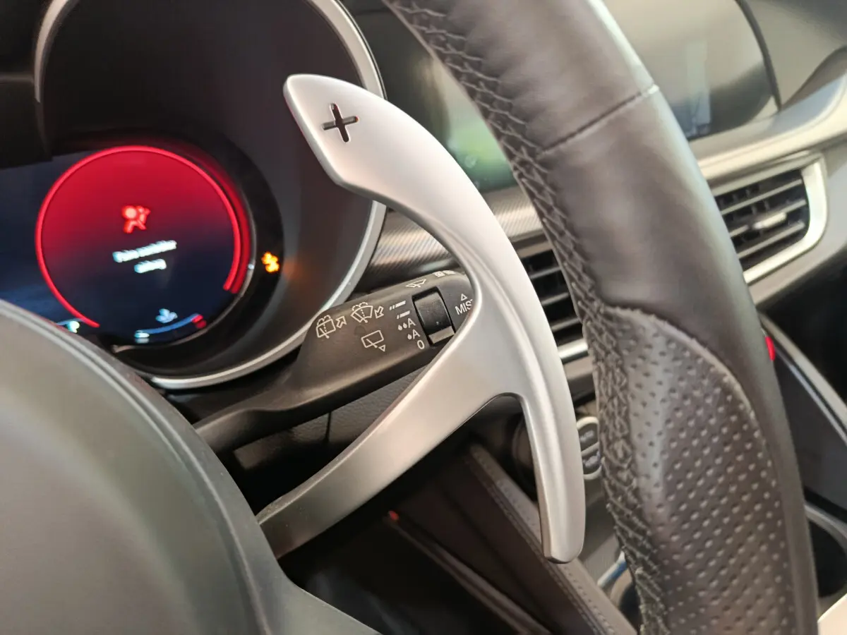 Gros plan sur la palette de changement de vitesse alu et cuir du volant de l'Alfa Romeo Stelvio gris foncé 2024.