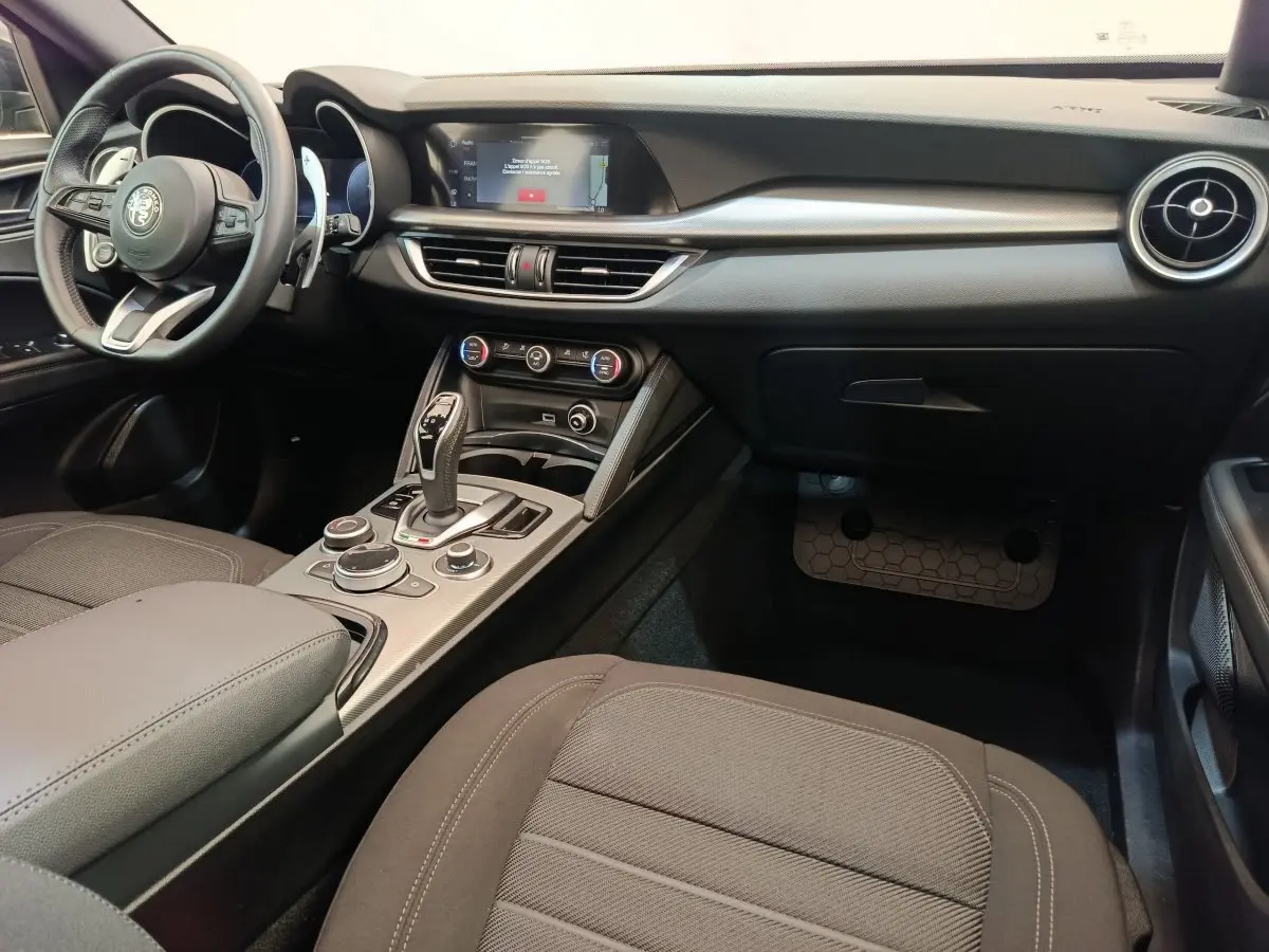 Intérieur noir de l'Alfa Romeo Stelvio 2024, vue côté passager avec console centrale et écran tactile visible.