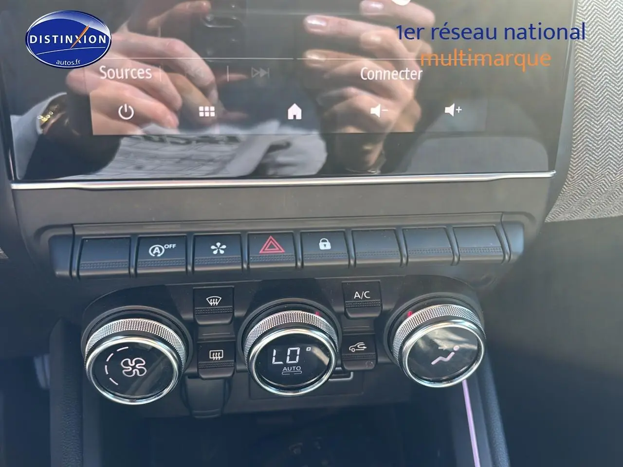 Gros plan sur la console centrale de la Renault Clio V gris pizzara, montrant les commandes de climatisation et les boutons fonctionnels.