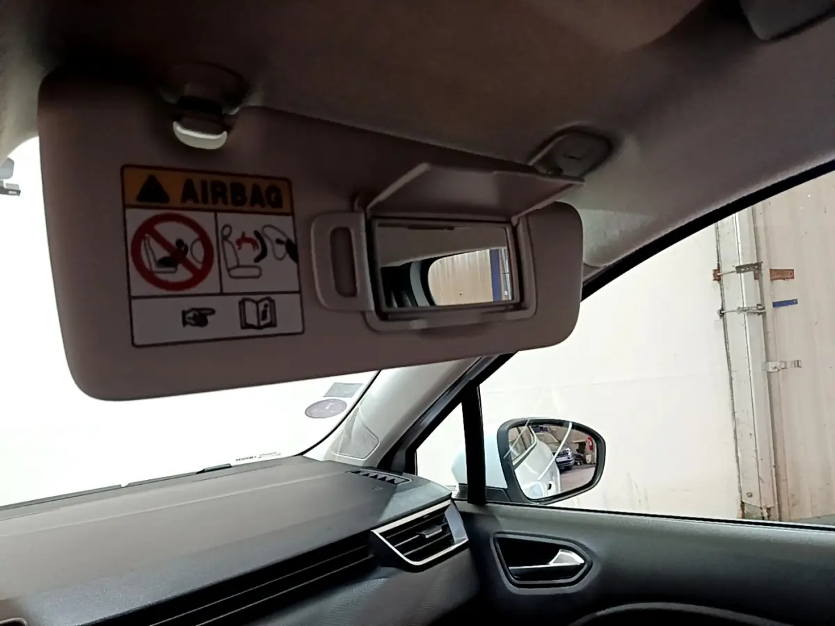Détail de l'intérieur côté passager d'une Renault Clio blanche 2021, avec pare-soleil ouvert et miroir visible.