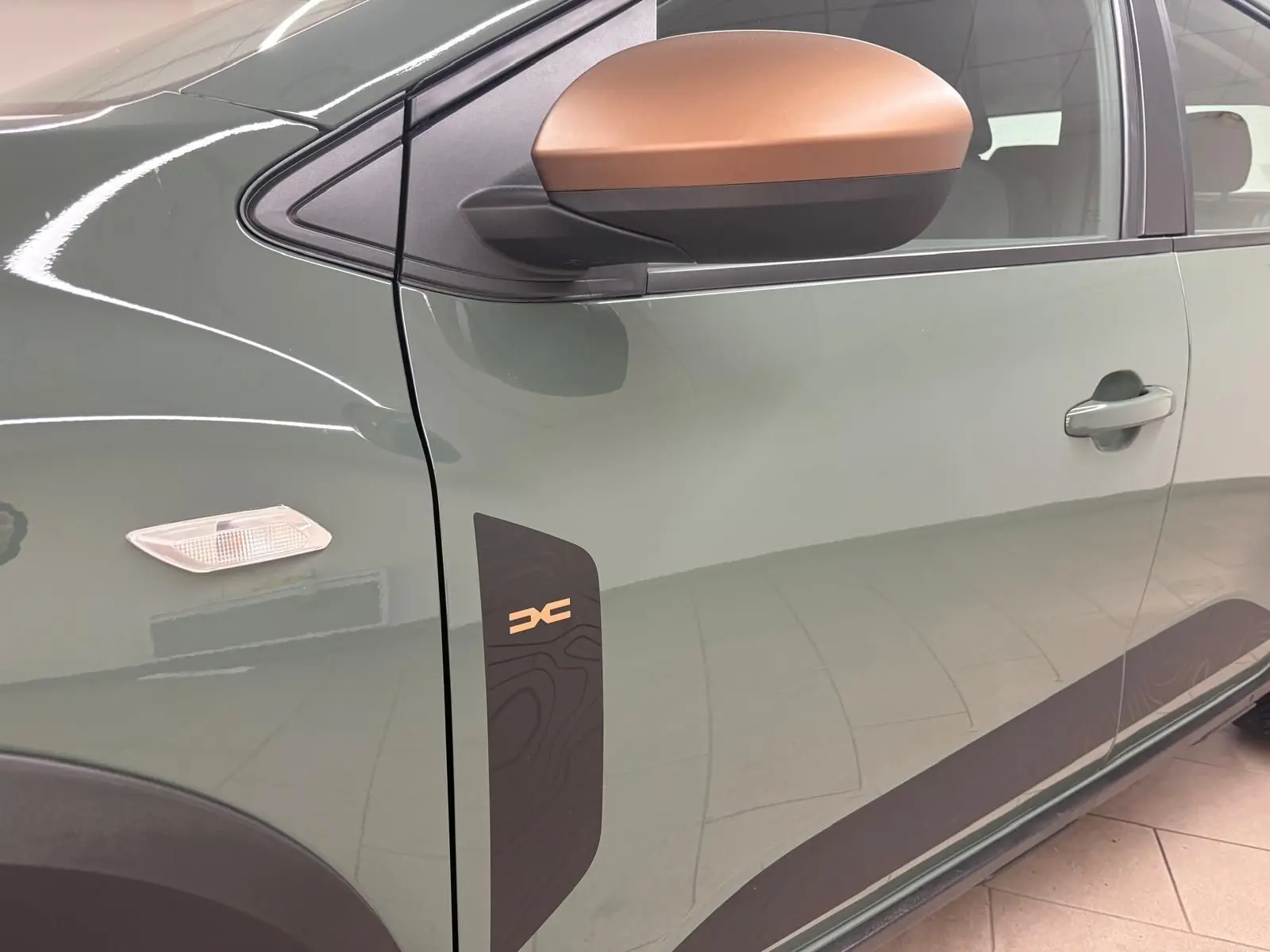 Vue latérale côté gauche du Dacia Sandero Stepway 2023 en vert cèdre, avec rétroviseur bronze et logo Stepway sur la porte.