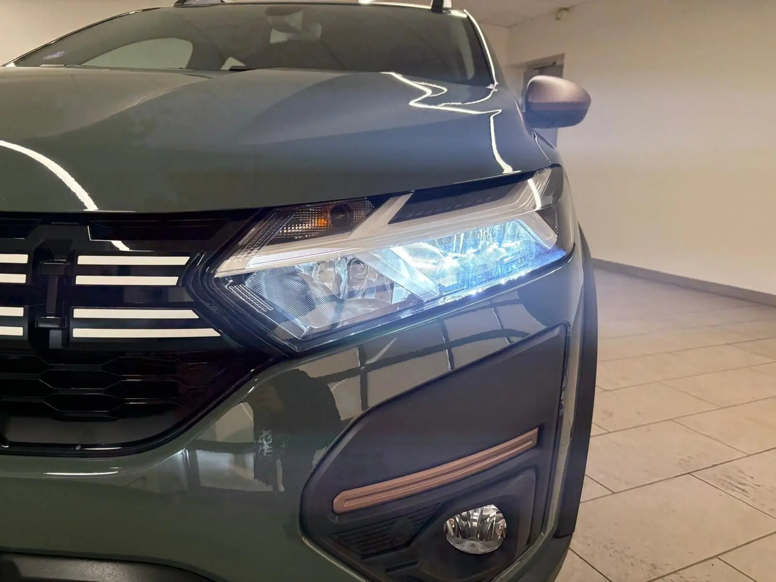 Gros plan sur l'avant droit vert cèdre du Dacia Sandero Stepway 2023 avec phare allumé et calandre noire.