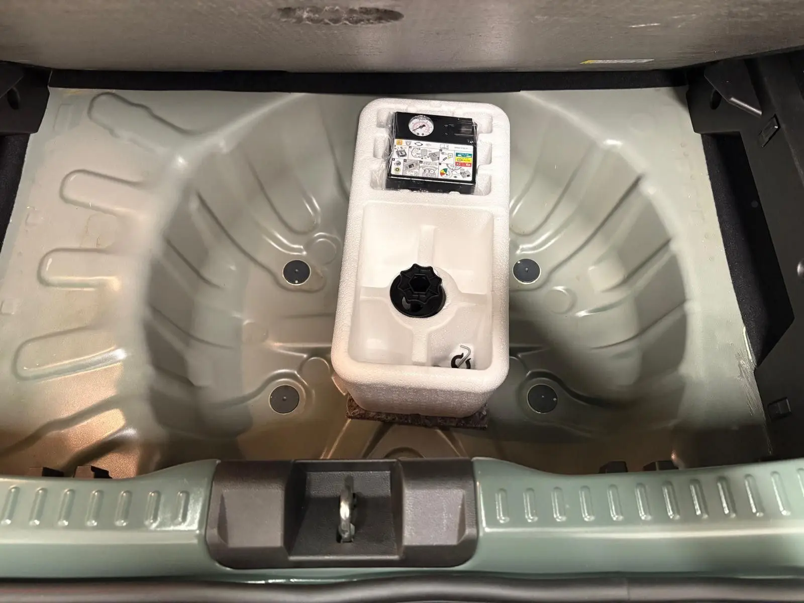 Coffre ouvert vu de dessus d’une Dacia Sandero Stepway 2023 vert cèdre, montrant le rangement sous plancher avec kit de réparation.