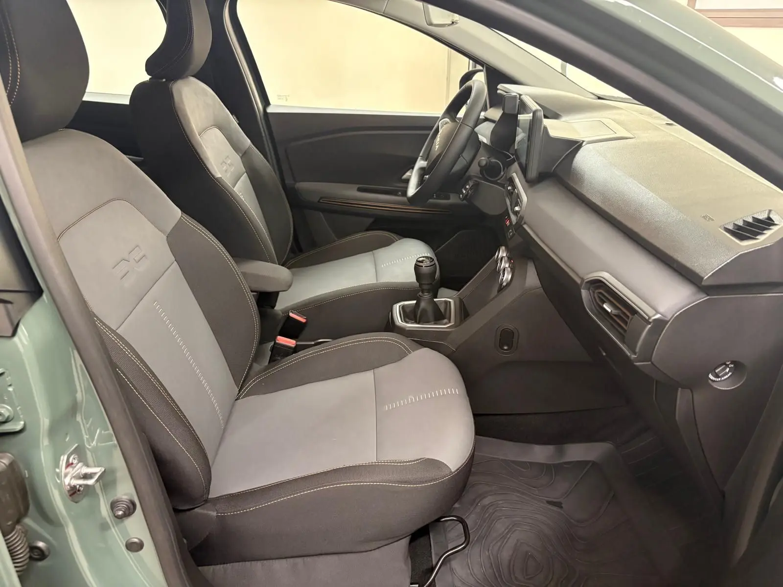 Vue intérieure côté gauche de la Dacia Sandero Stepway 2023 vert cèdre, montrant les sièges et la console avec boîte manuelle.