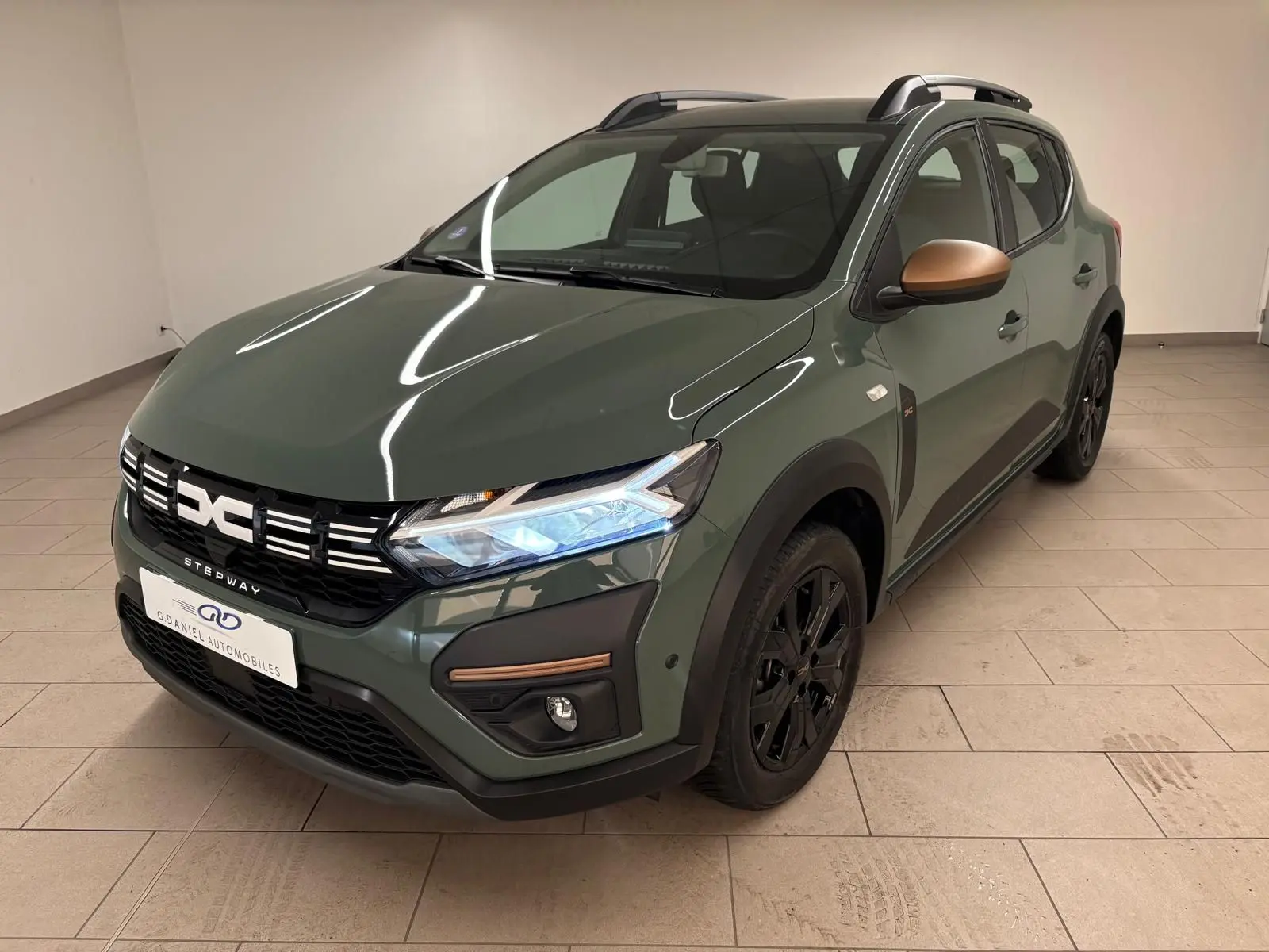 Vue 3/4 avant droite d'une Dacia Sandero Stepway 2023 vert cèdre avec rétroviseurs bronze et jantes noires.