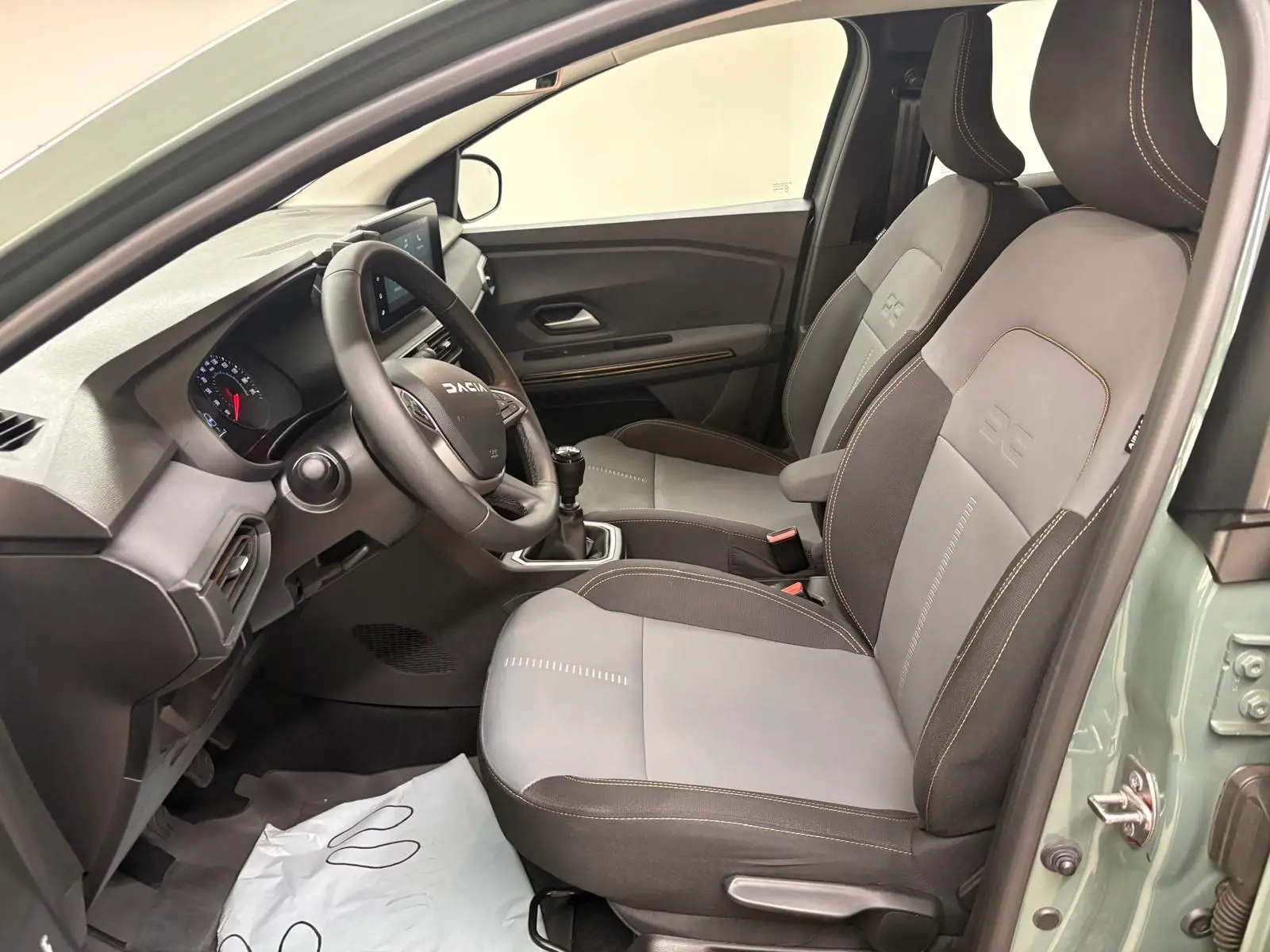 Vue intérieure côté conducteur de la Dacia Sandero Stepway 2023 vert cèdre, sièges bi-ton gris avec surpiqûres contrastées.