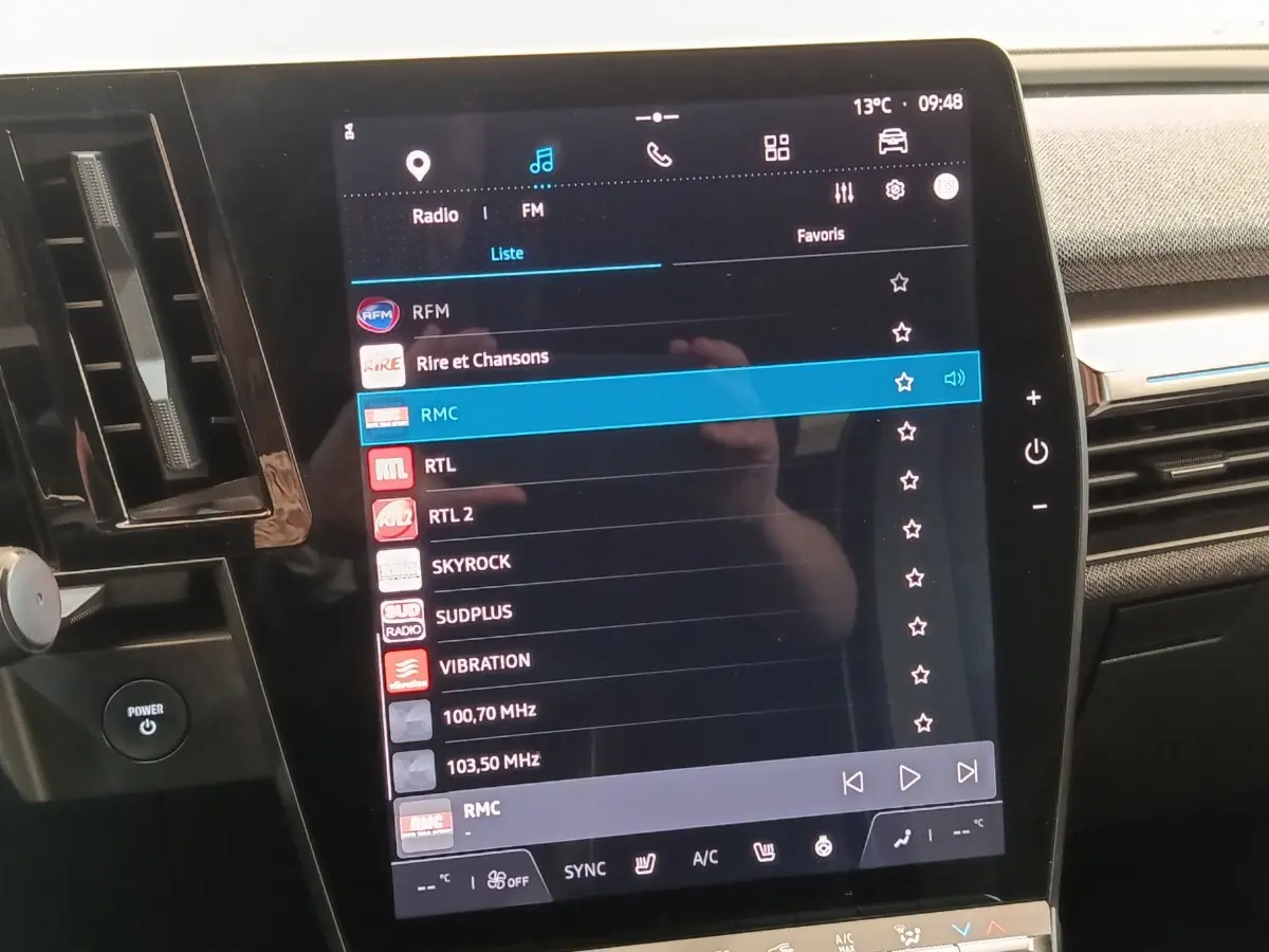 Vue rapprochée de l’écran tactile central de la Renault Mégane Techno EV60 bleu, affichant les stations radio FM.