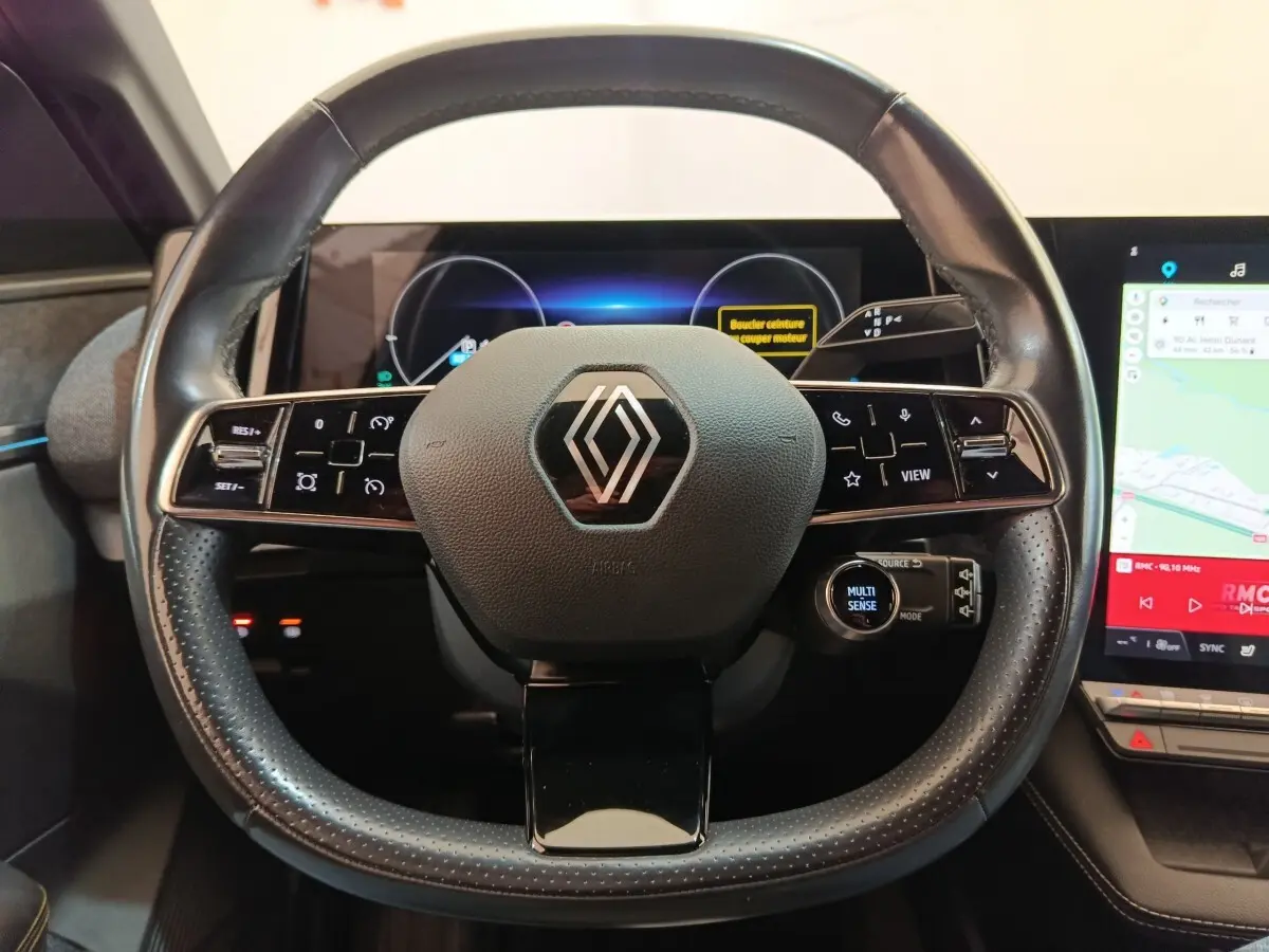 Vue rapprochée du volant cuir noir de la Renault Mégane électrique 2023 avec commandes multifonctions et écran tactile.