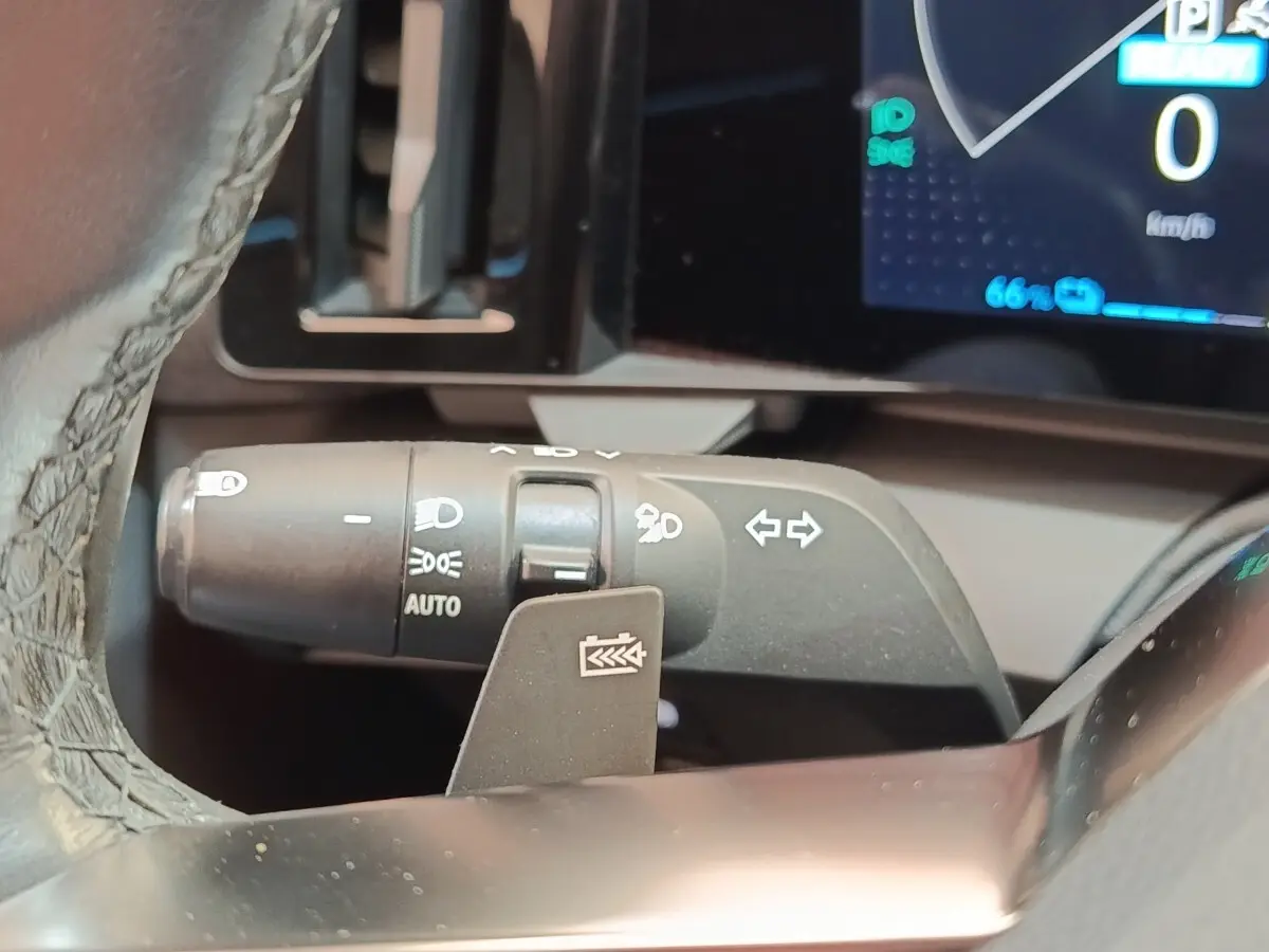 Gros plan sur la commande des feux et clignotants à gauche du volant dans le tableau de bord numérique d’une Renault Mégane bleu électrique.