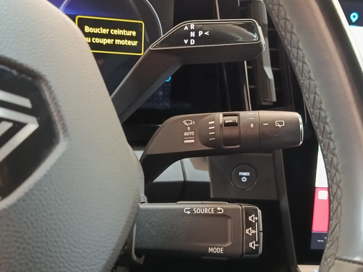 Gros plan sur les commandes au volant d’une Renault Mégane électrique bleu, affichage digital et bouton Power visibles.