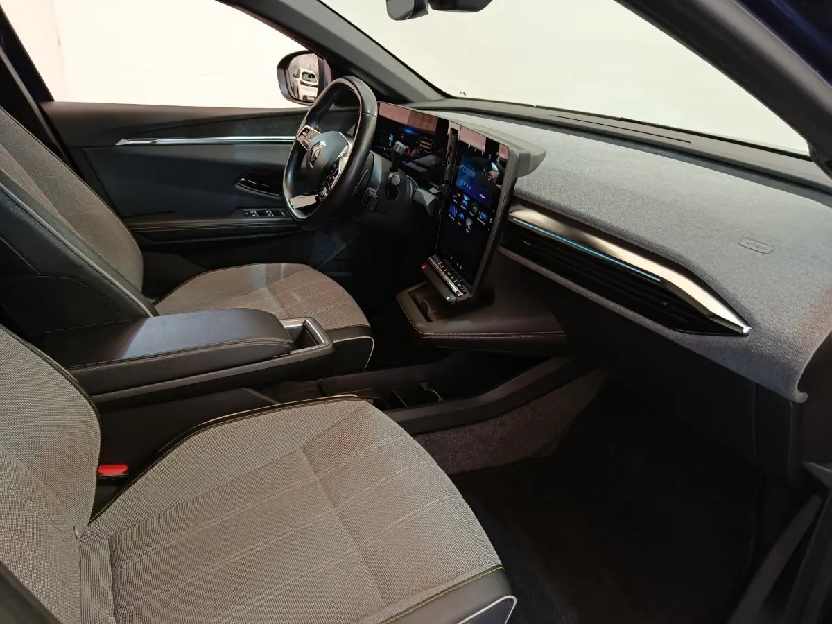 Intérieur avant droit de la Renault Mégane Techno EV60 220ch, sièges gris, grand écran tactile vertical et volant cuir.