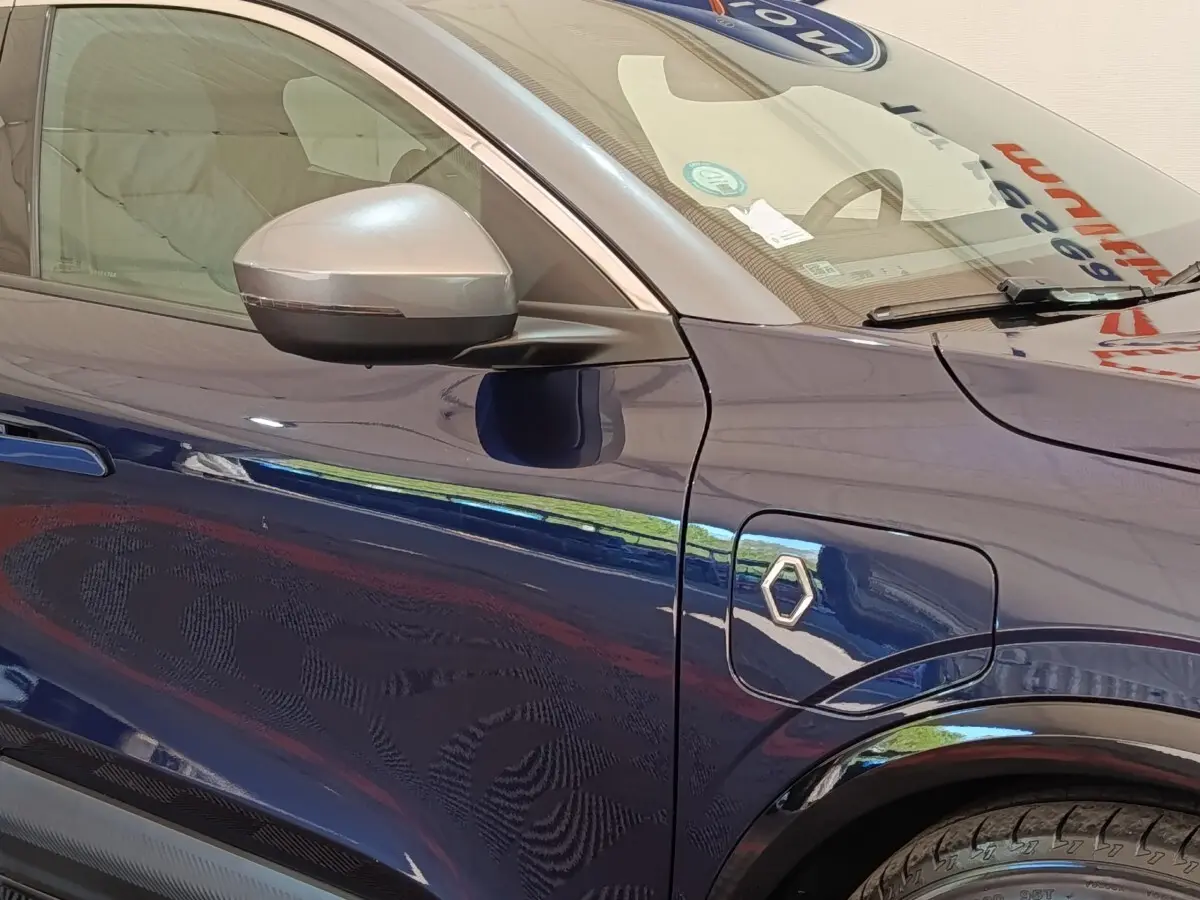 Vue latérale gauche rapprochée de la Renault Megane Techno EV60 bleu avec rétroviseur argenté et prise de recharge électrique.