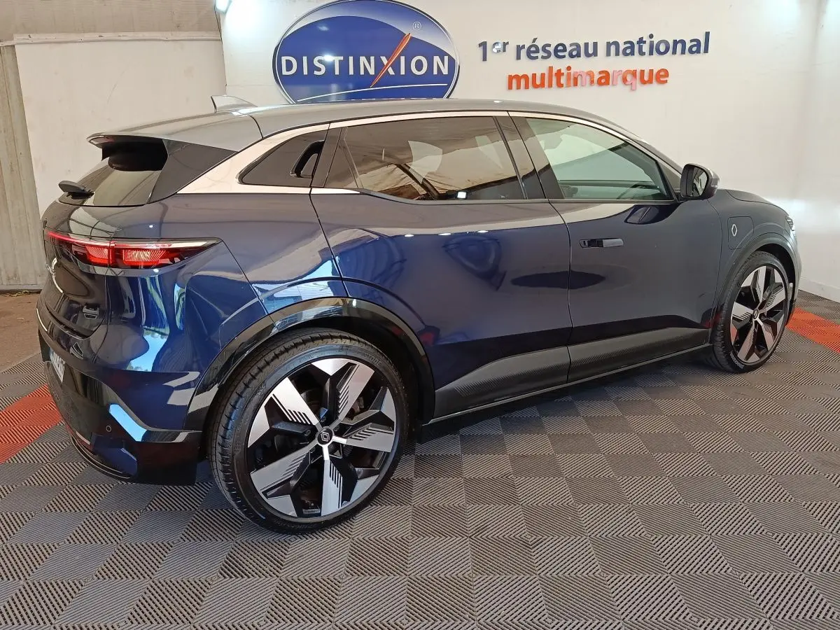 Renault Mégane Techno EV60 bleu en 3/4 arrière droit, jantes modernes et toit contrasté argenté visible en intérieur showroom.