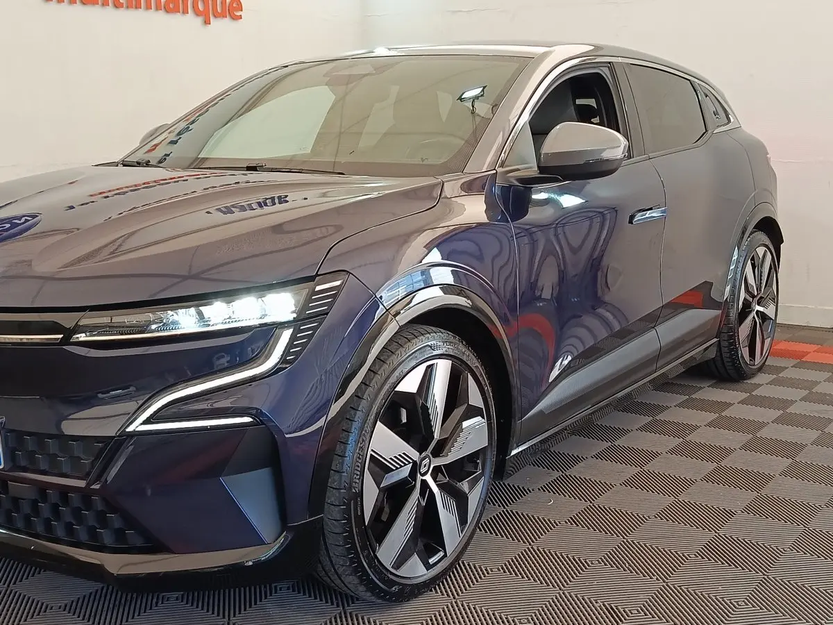 Vue 3/4 avant droit d'une Renault Mégane Techno EV60 bleu électrique avec phares LED allumés et jantes stylisées.