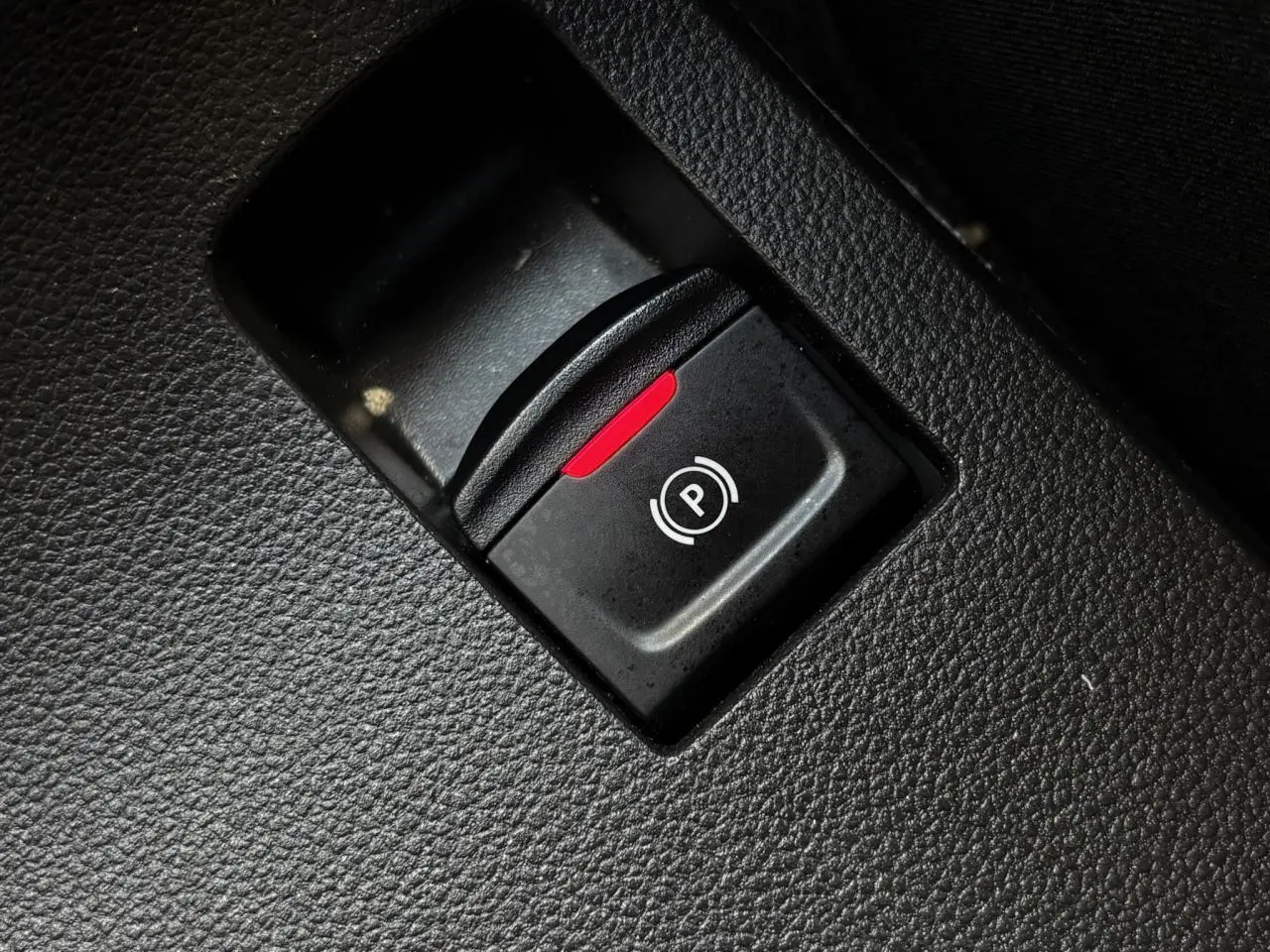Gros plan sur le bouton de frein de parking électrique avec témoin rouge dans l'habitacle noir du Dacia Sandero Stepway.