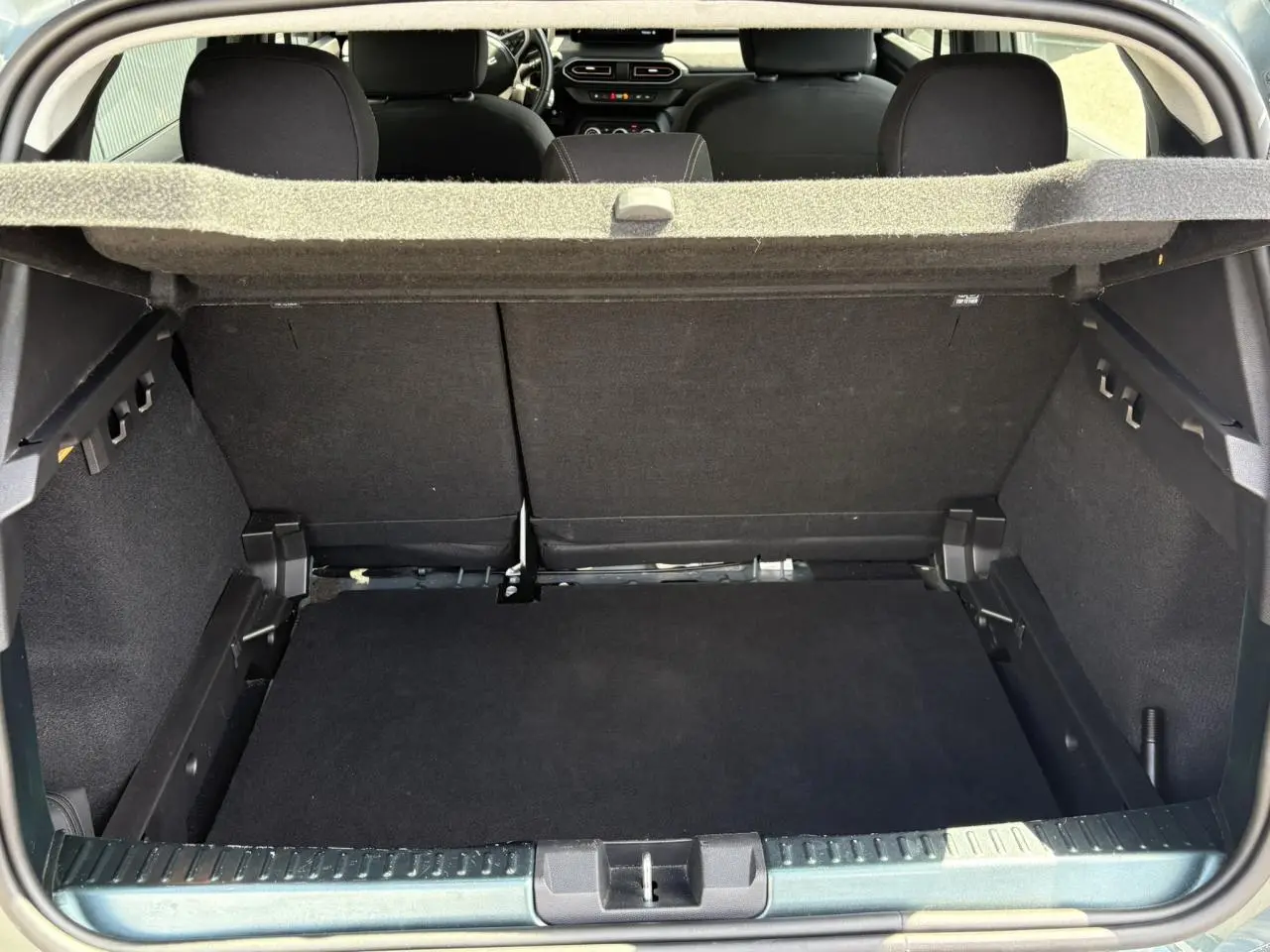 Coffre ouvert vu de l'arrière d'une Dacia Sandero Stepway Vert Cèdre, avec banquette arrière et cache-bagages visibles.