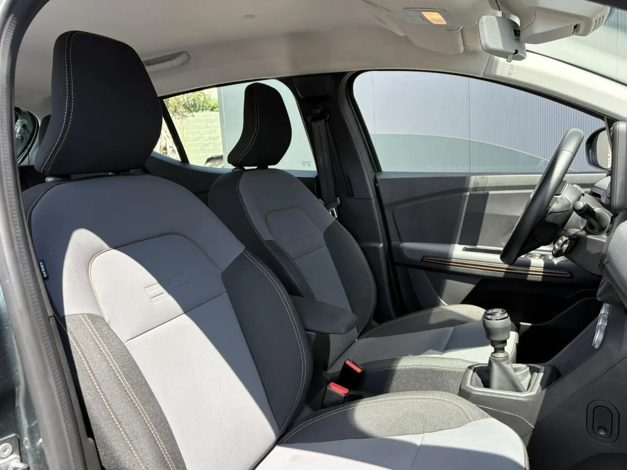 Vue intérieure côté conducteur de la Dacia Sandero Stepway 2025 avec sièges gris et accoudoir central.