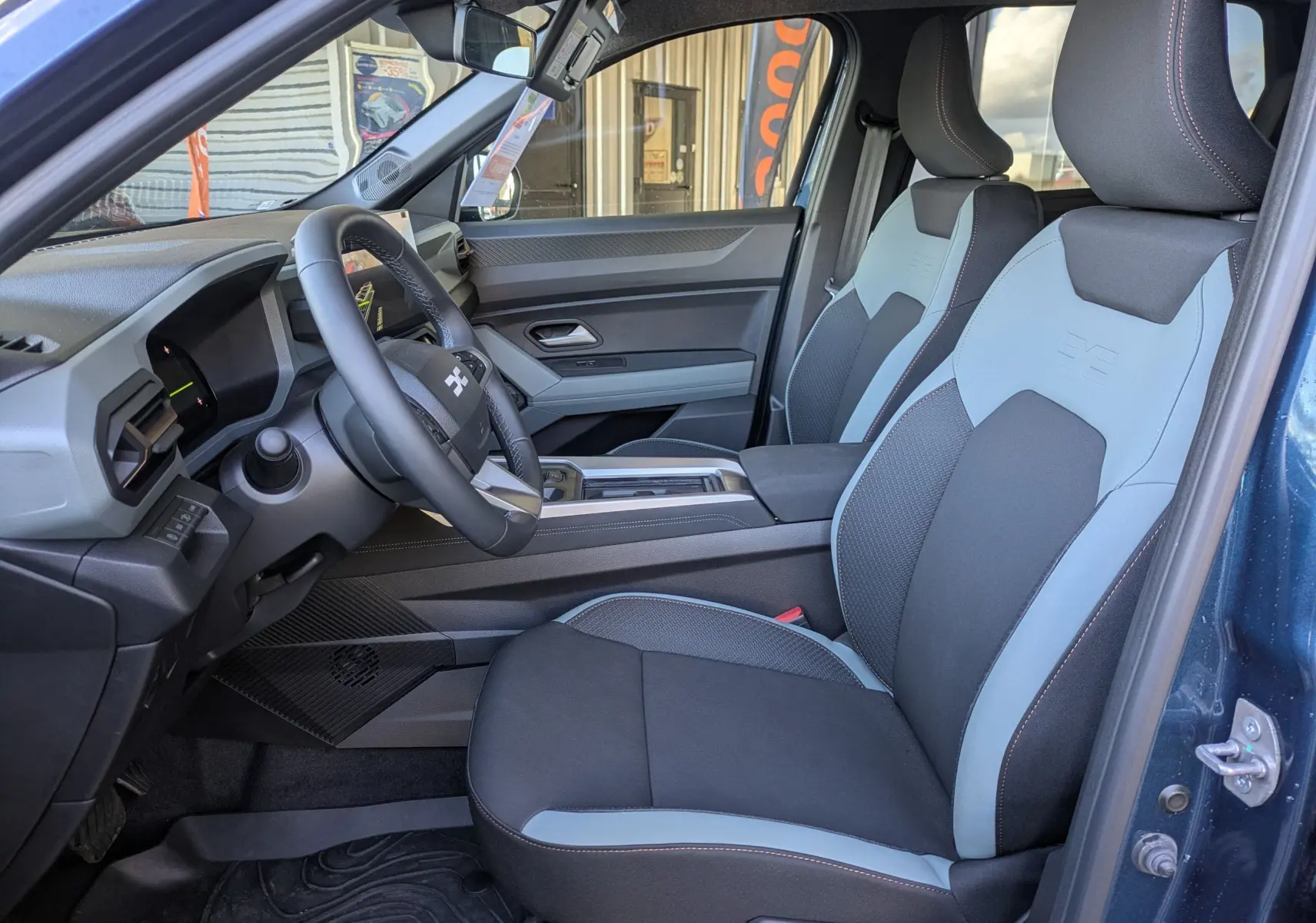 Vue intérieure côté conducteur du Dacia Bigster Hybrid 155 Extreme bleu indigo, sièges bi-ton gris et noir avec surpiqûres.