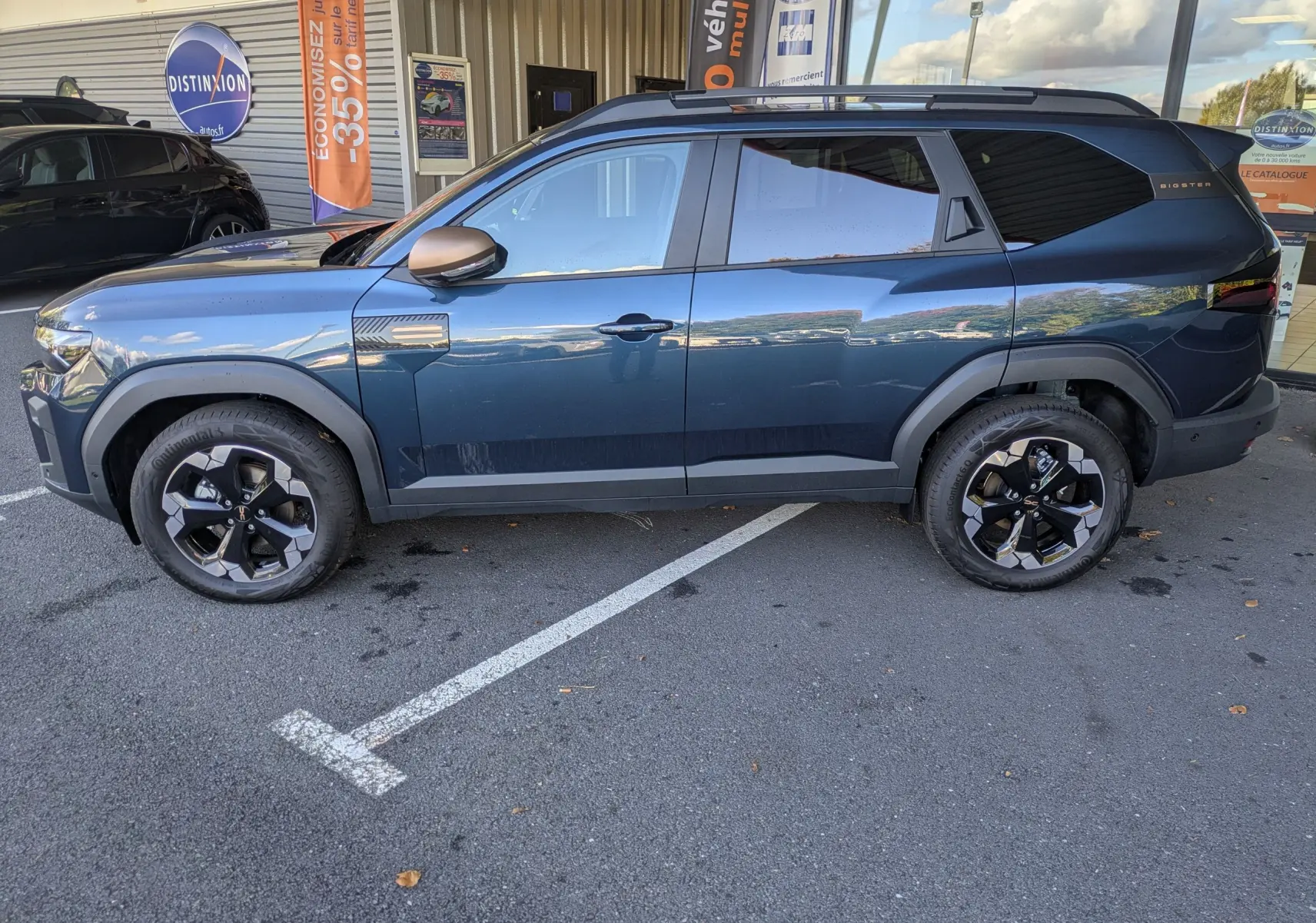 Vue latérale droite d'un Dacia Bigster Hybrid 155 Extreme bleu indigo avec jantes alliage bicolores et barres de toit.
