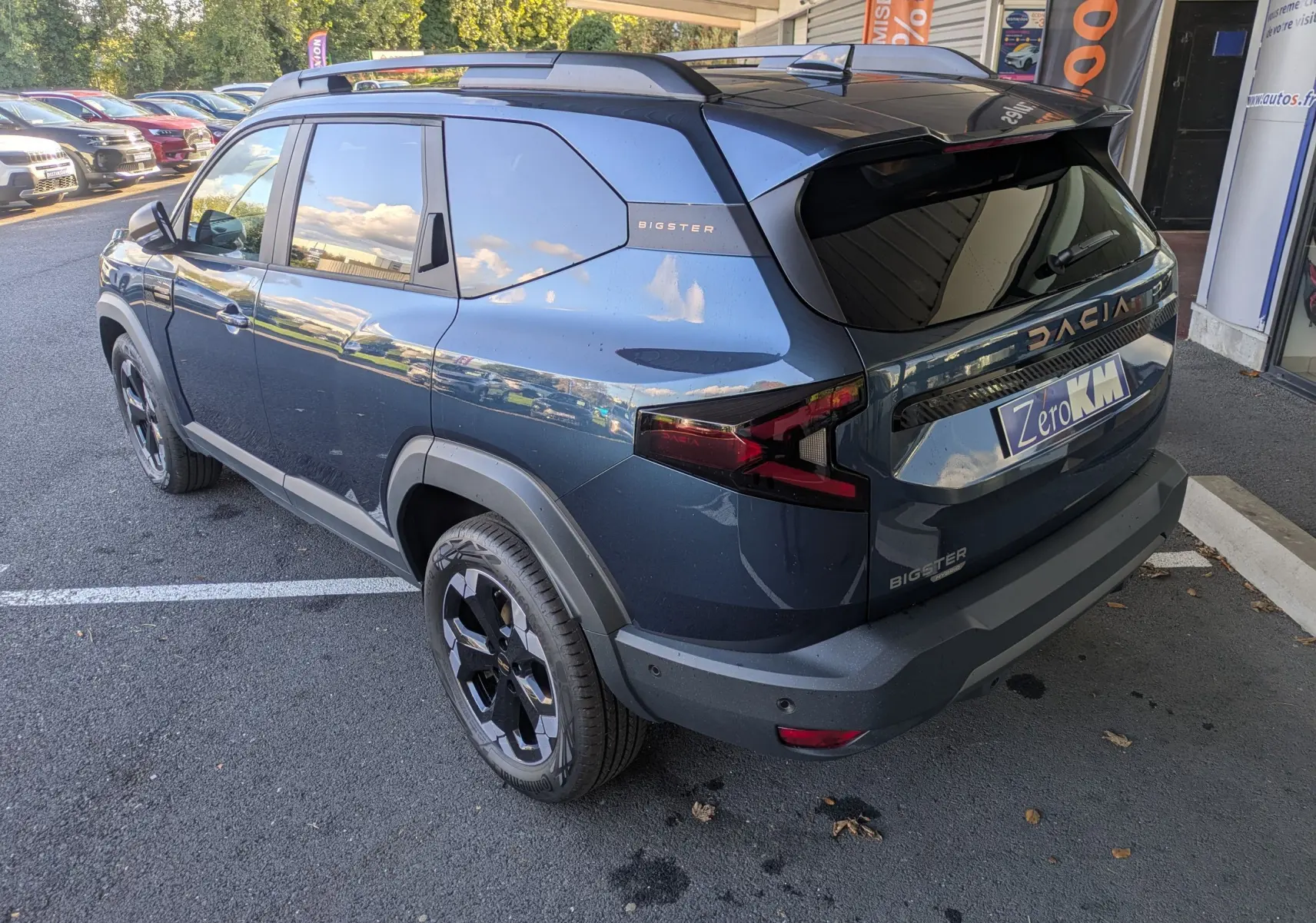 Vue 3/4 arrière droite du Dacia Bigster Hybrid 155 Extreme bleu indigo avec jantes noires et barres de toit.