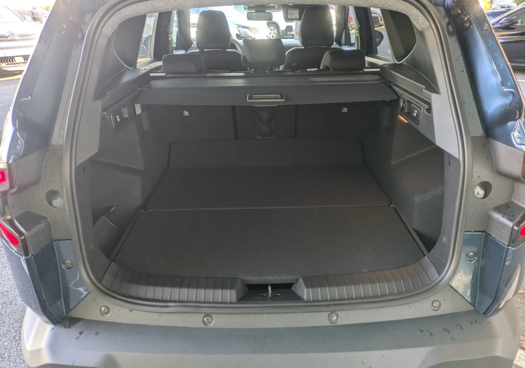 Coffre ouvert vu de l'arrière du Dacia Bigster Hybrid 155 Extreme bleu indigo, montrant l'espace de chargement avec cache-bagages.