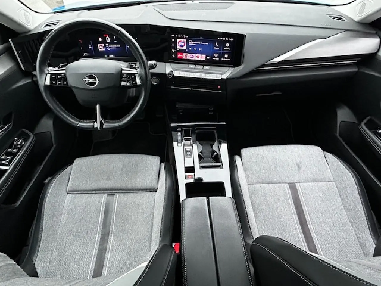 Vue intérieure avant de l'Opel Astra VI 2022, avec tableau de bord numérique et sièges tissu gris clair.