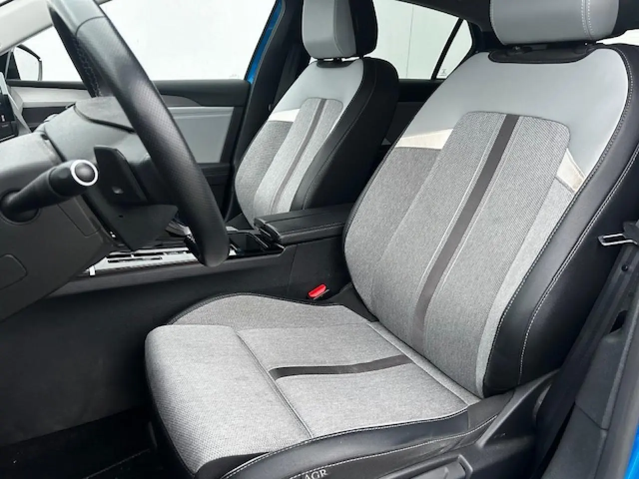 Vue intérieure côté conducteur de l'Opel Astra bleu clair 2022, sièges tissu gris avec surpiqûres noires et volant cuir Premium.
