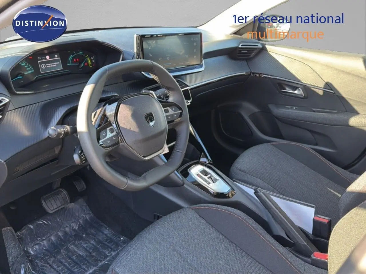 Intérieur avant droit de la Peugeot 208 1.2 Hybrid 2025 avec volant compact, écran tactile et sièges tissu gris.