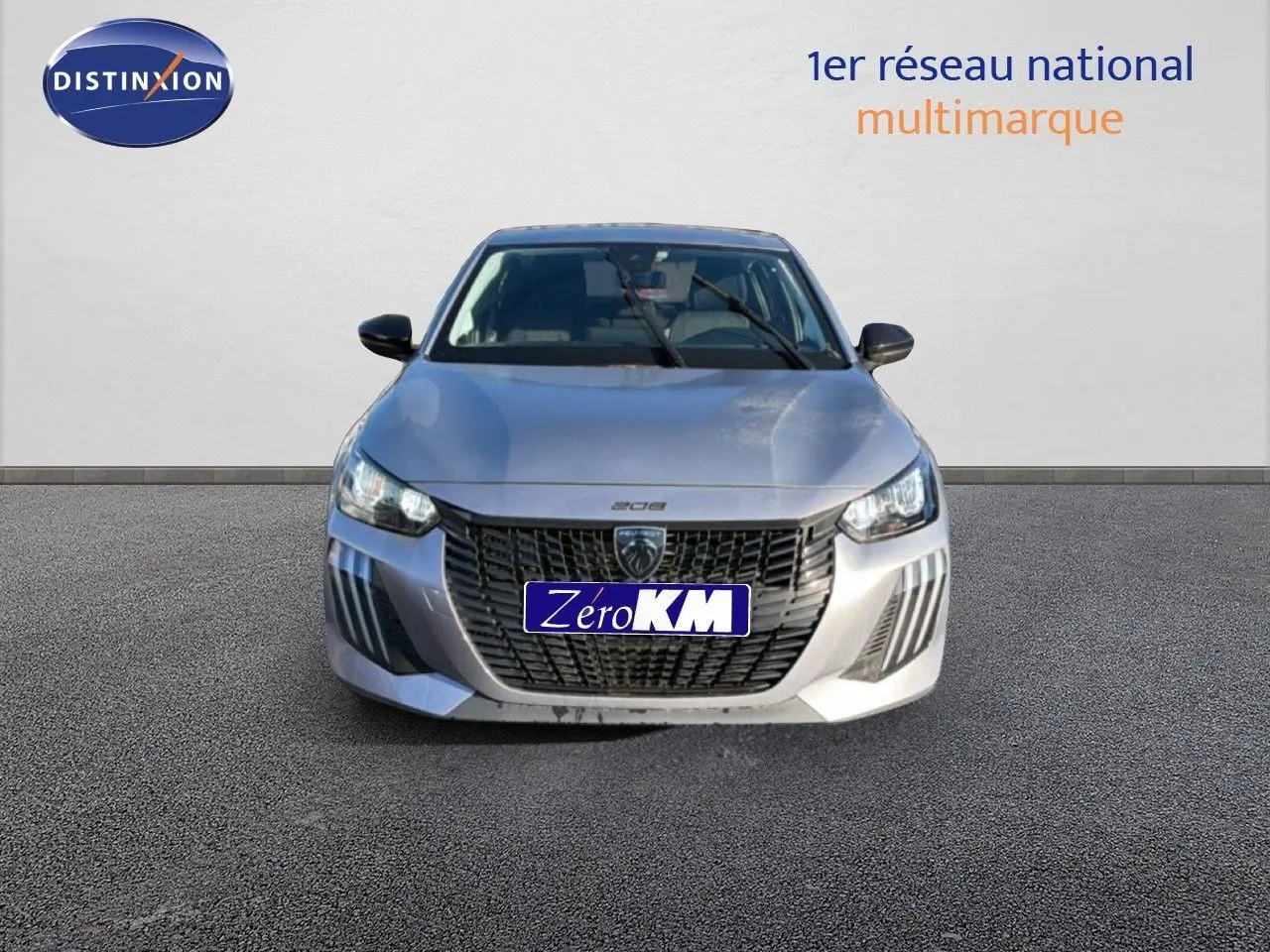 Vue frontale d'une Peugeot 208 gris artense métal 2025 avec calandre noire et phares LED allumés.