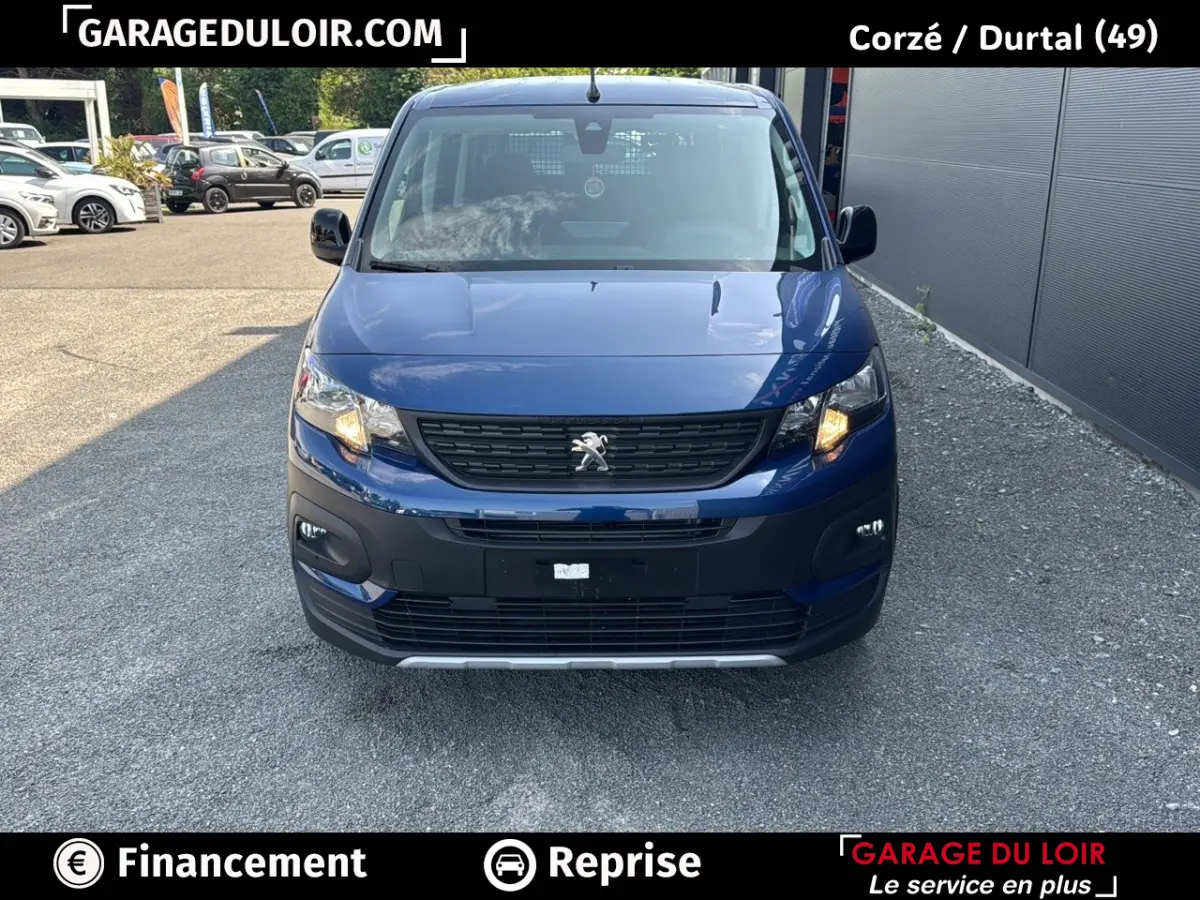 Vue avant d'un Peugeot Rifter bleu 2024 avec calandre noire et feux allumés sur un parking extérieur.