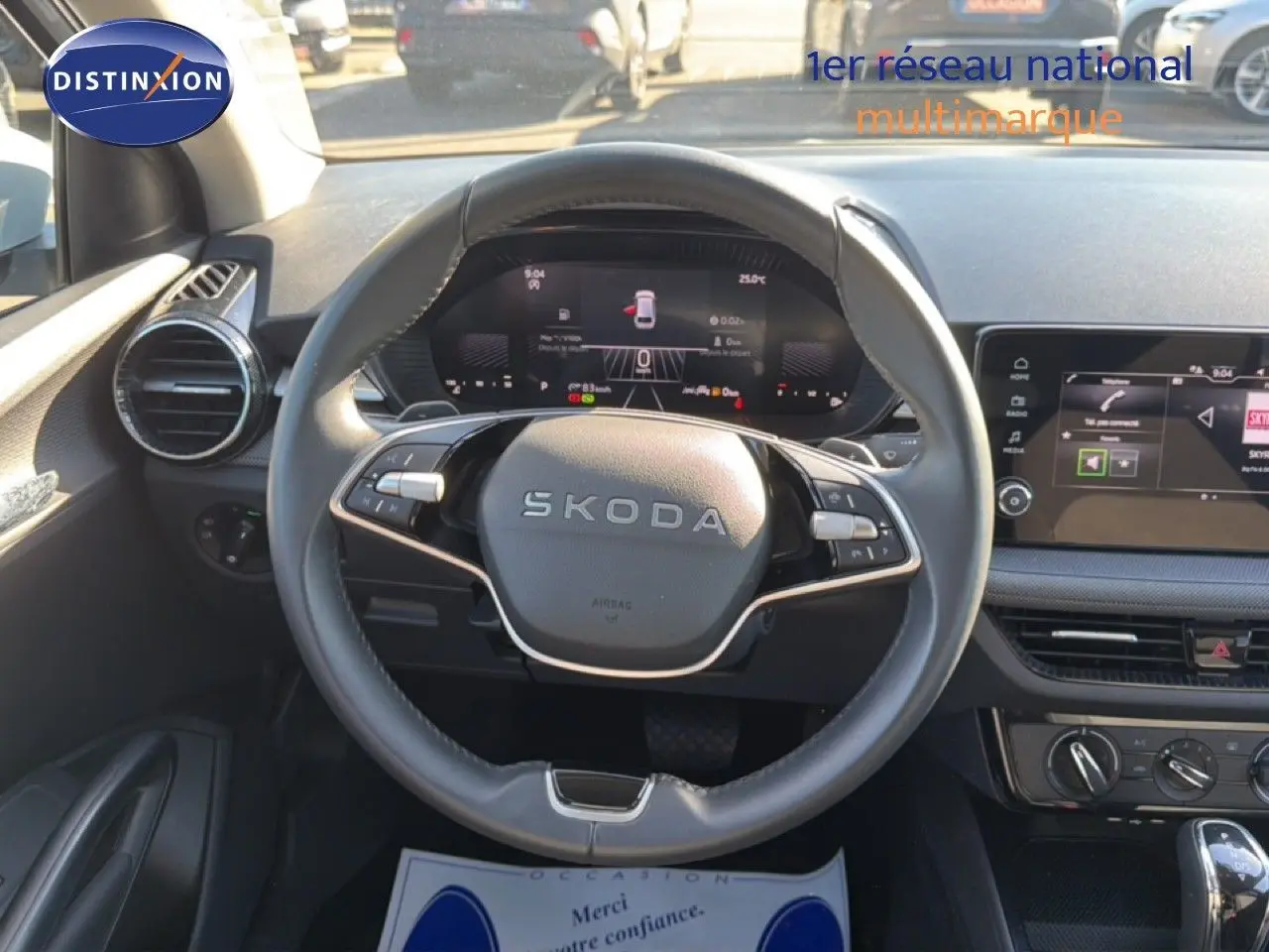 Vue intérieure centrée sur le volant SKODA d'une Fabia blanche, avec tableau de bord digital et écran tactile visible.