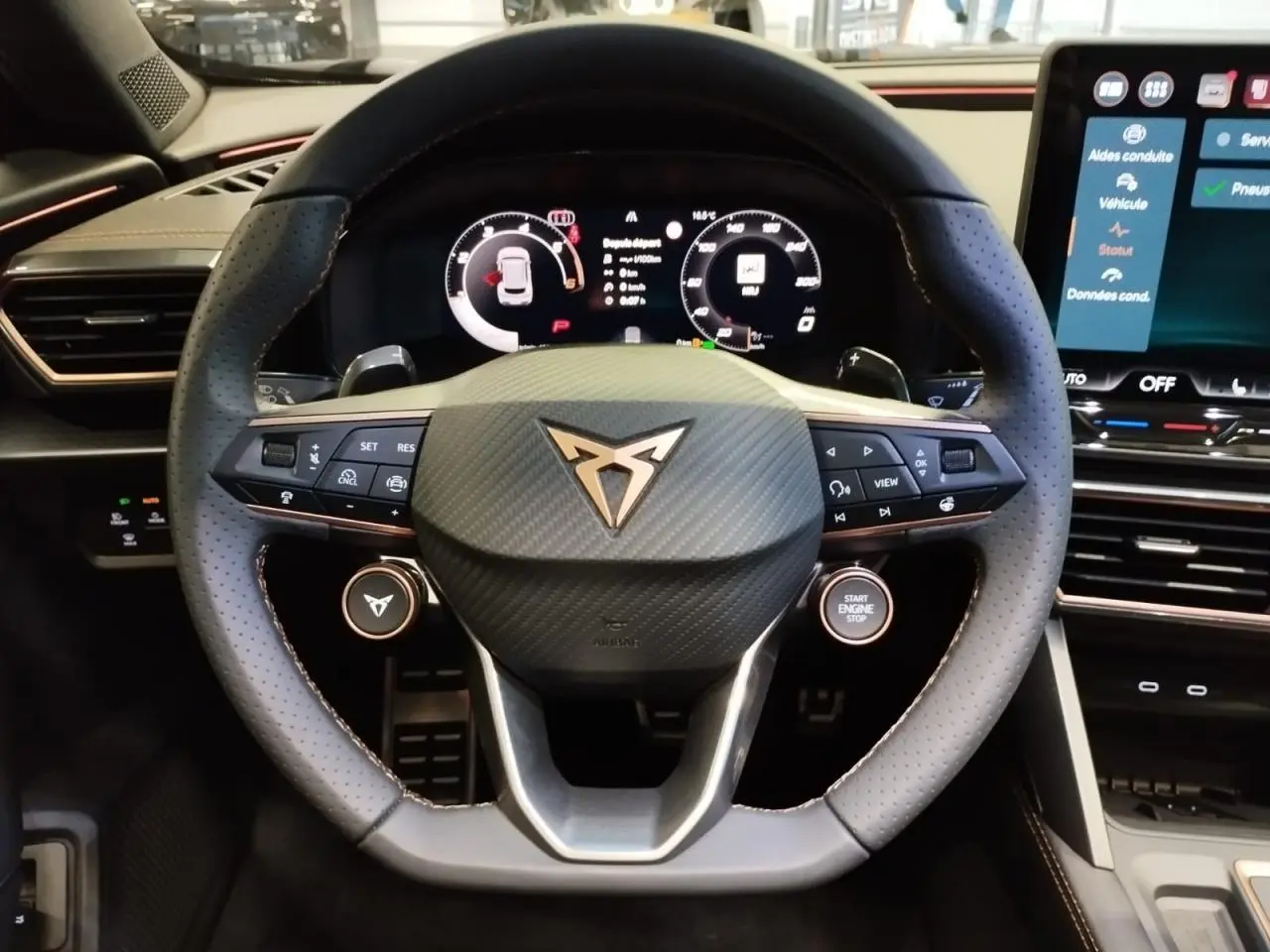 Volant Cupra en cuir perforé noir avec logo cuivré, vue frontale du poste de conduite digital et écran tactile HD.