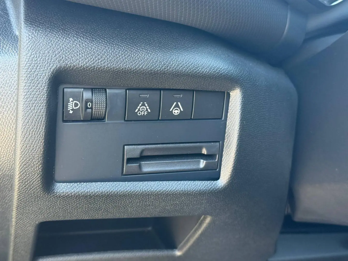 Gros plan sur les commandes de réglage des phares et d'aides à la conduite dans l'habitacle noir du Citroën C5 Aircross.