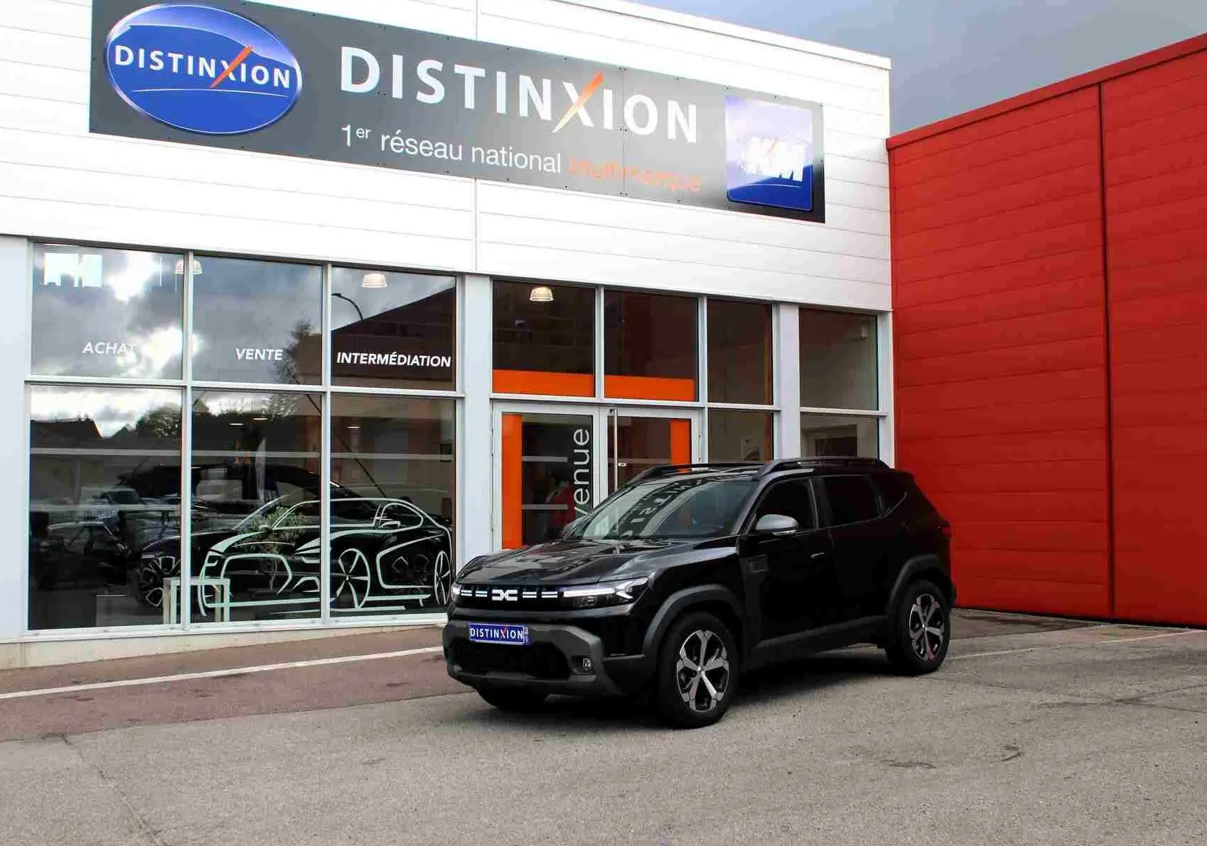 Dacia Duster III noir nacré vu en 3/4 avant droit devant un bâtiment commercial Distinxion.