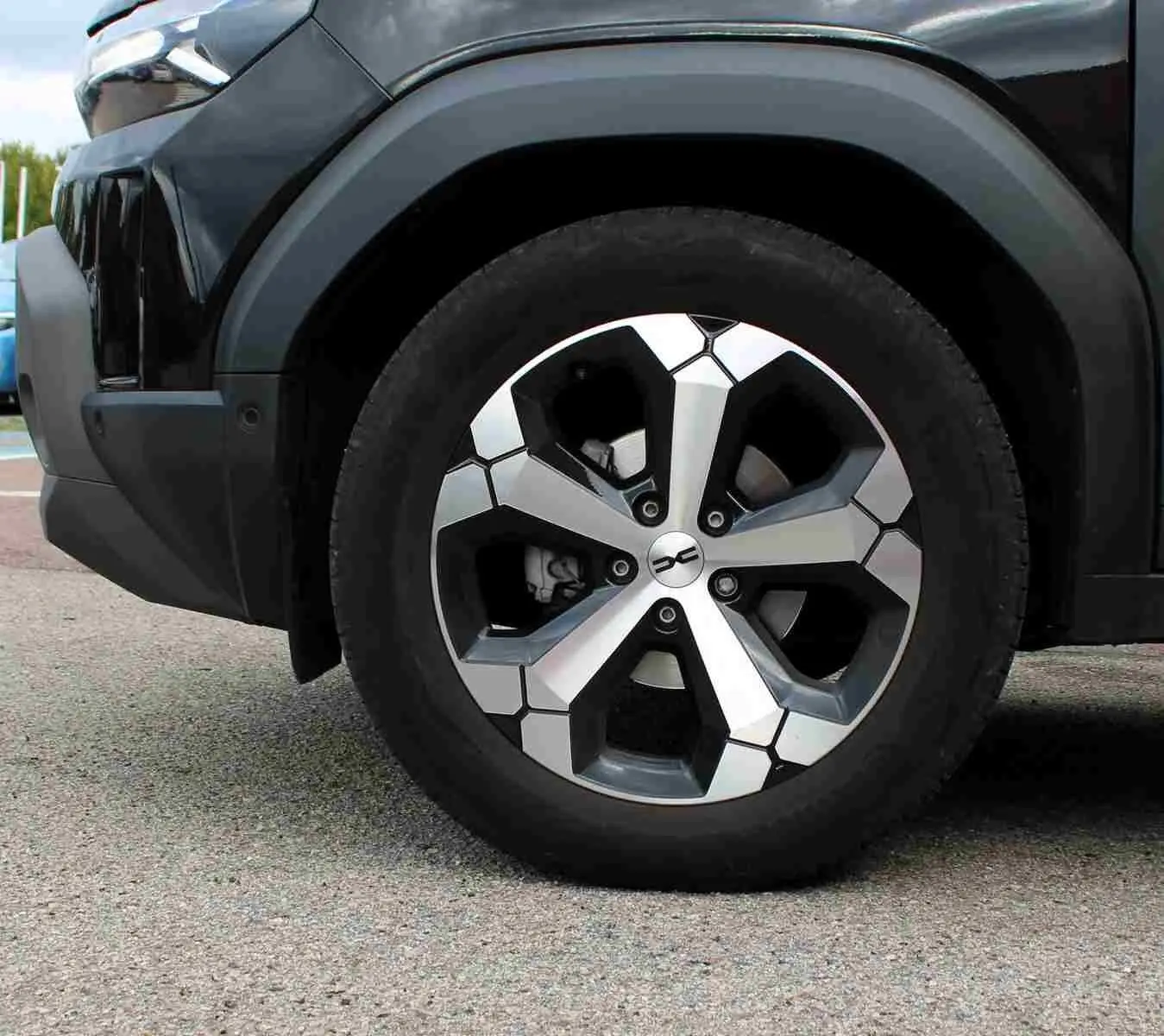 Gros plan sur la roue avant gauche du Dacia Duster noir 2025 avec jante alliage 18 pouces diamantée Tagasan.