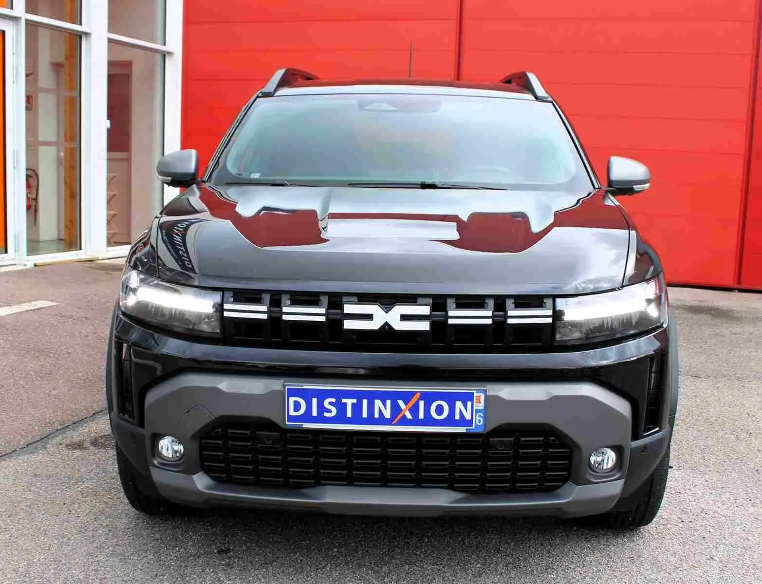 Vue frontale d'un Dacia Duster III noir nacré avec calandre distinctive et plaques d'immatriculation Distinxion.