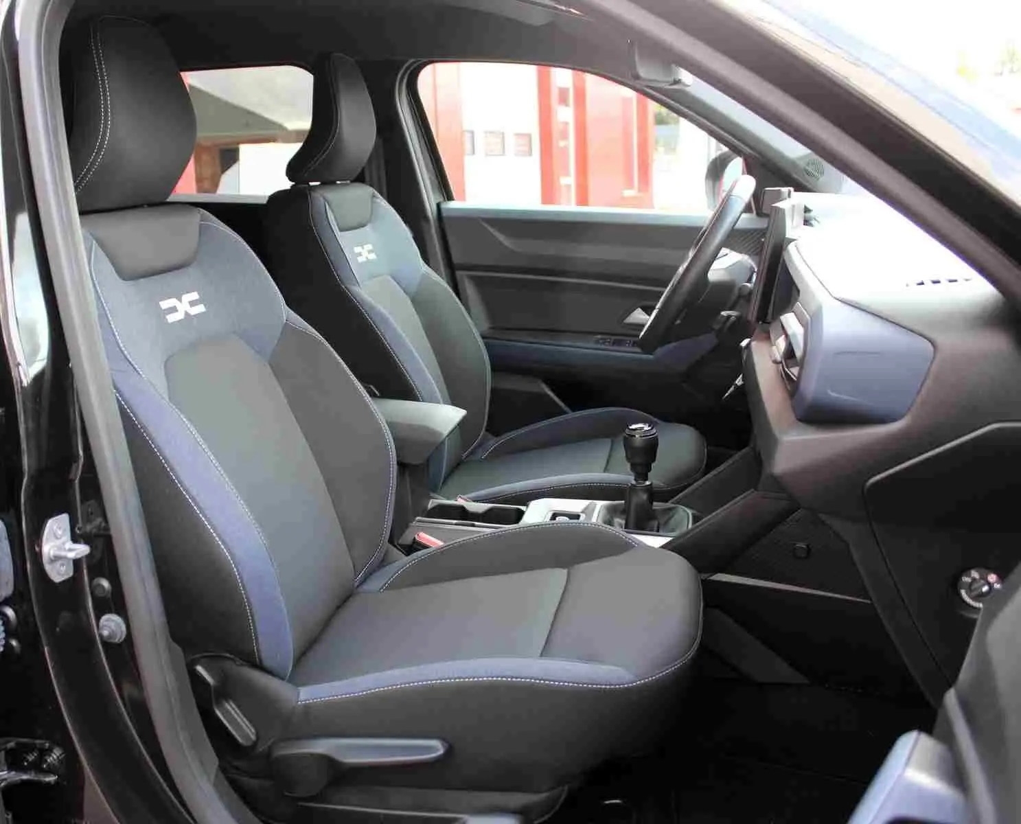 Vue intérieure côté gauche du Dacia Duster III noir, mettant en valeur les sièges avant Denim avec logo Dacia.