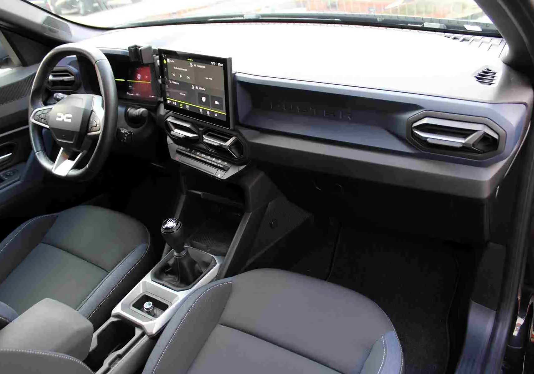 Intérieur du Dacia Duster III noir, vue côté conducteur, tableau de bord avec écran tactile et volant multifonction.