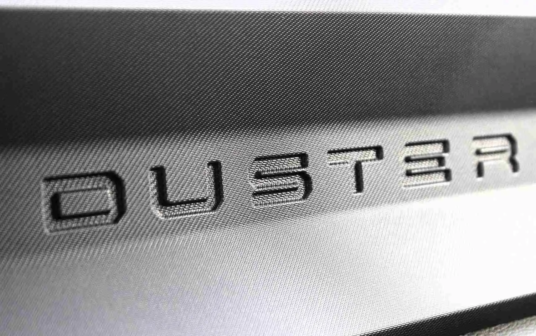 Gros plan sur le logo DUSTER en relief sur une surface intérieure grise du Dacia Duster noir.