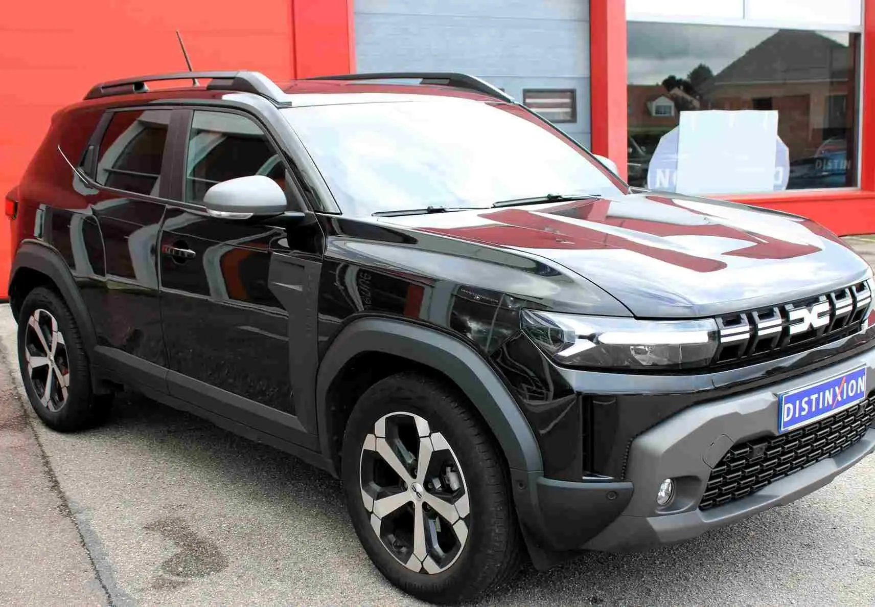 Dacia Duster noir nacré en 3/4 avant droit, avec jantes alliage 18 pouces et barres de toit noires.