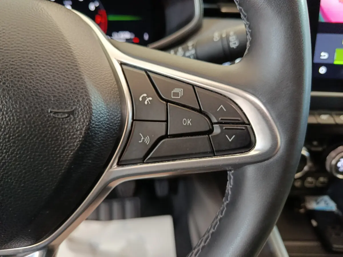 Gros plan sur les commandes du volant cuir noir de la Renault Clio Techno TCe 90, avec écran tactile en arrière-plan.