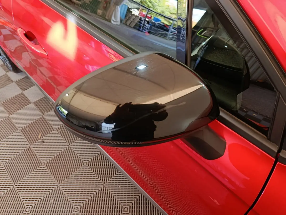 Rétroviseur noir côté gauche en gros plan sur Renault Clio rouge 2024, avec poignée de porte visible.