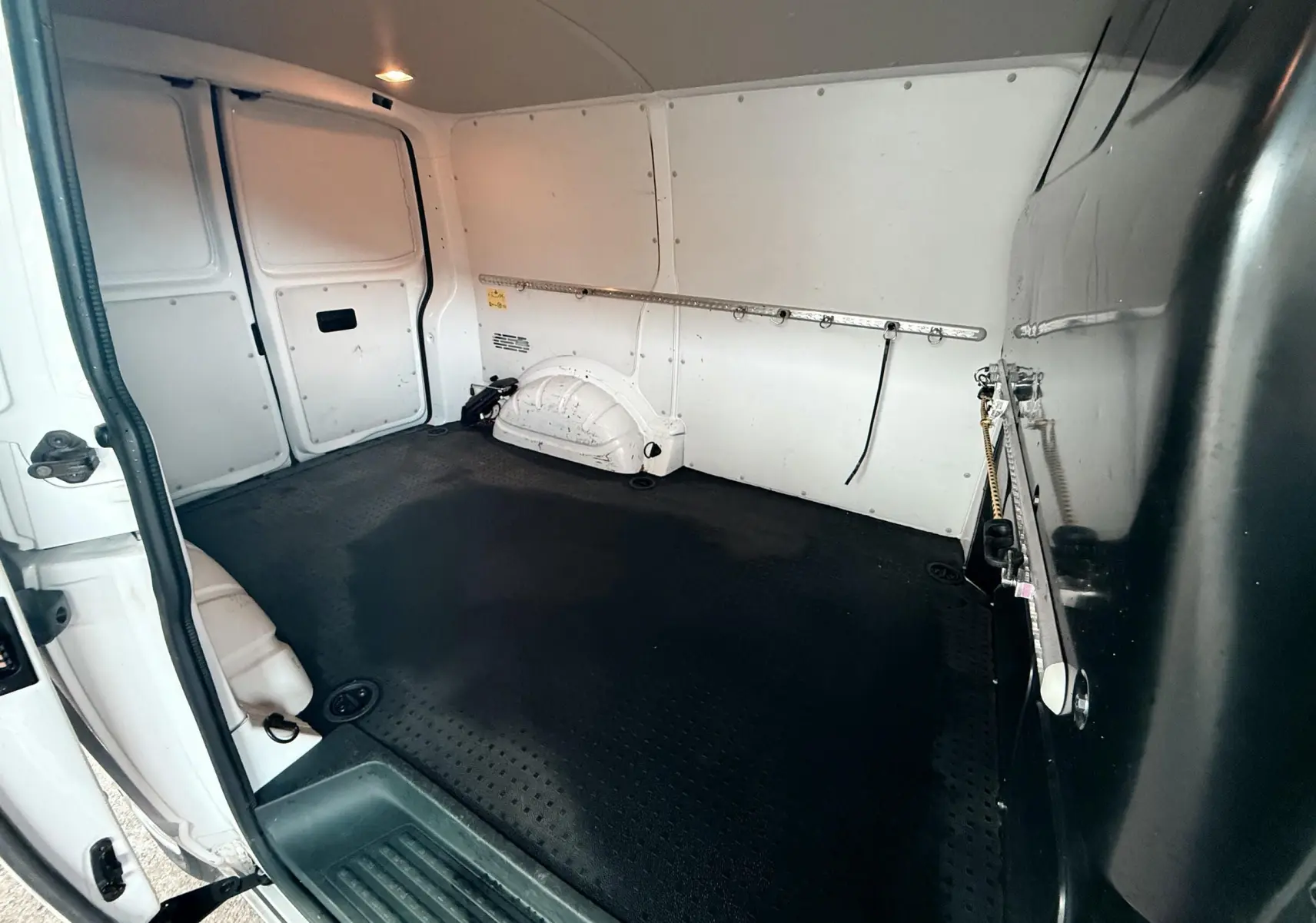 Vue intérieure arrière du Volkswagen Transporter L1H1 blanc de 2018, montrant l’espace de chargement vide avec revêtement noir.